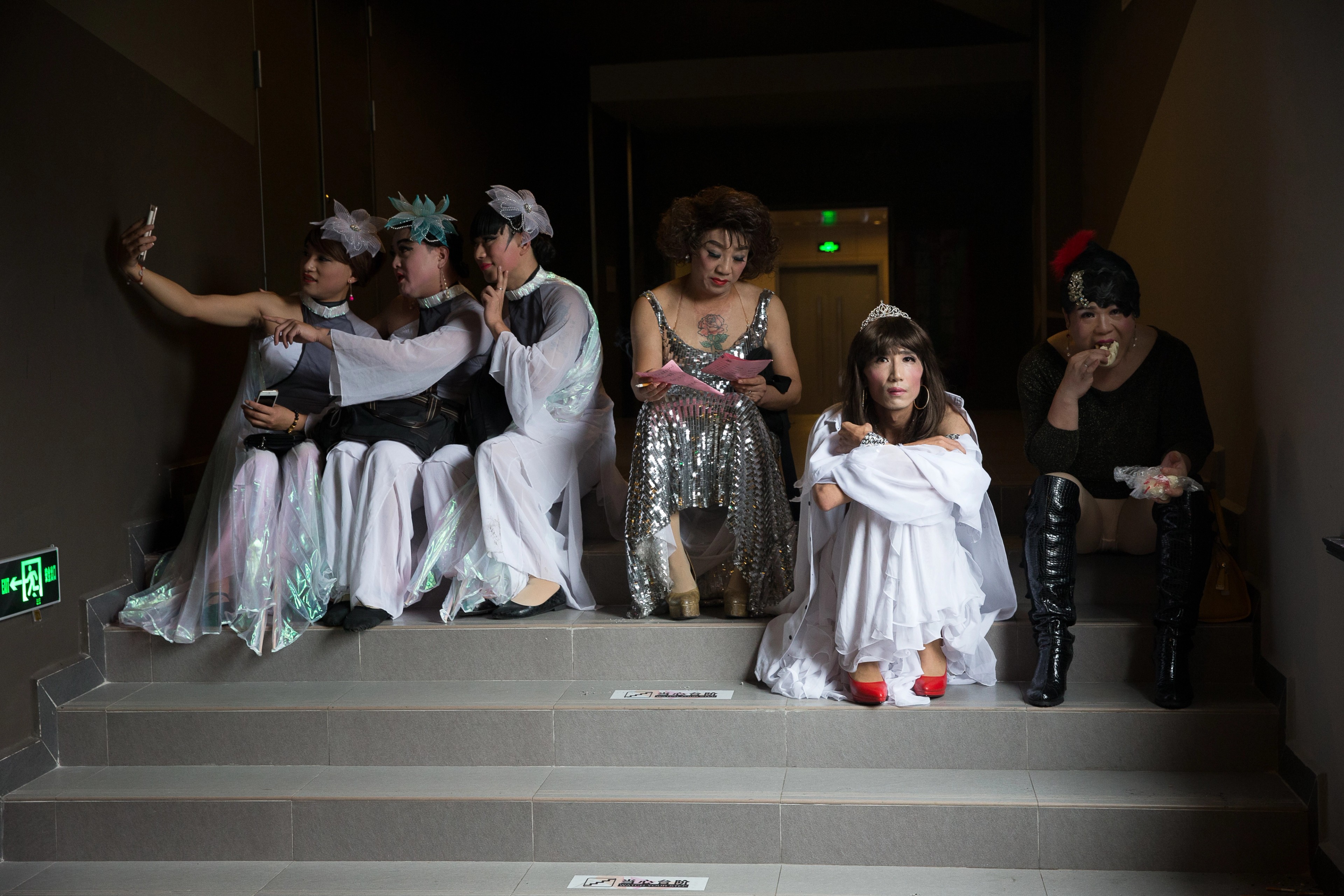 A group of performers in elaborate costumes sitting together on a stairwell backstage.