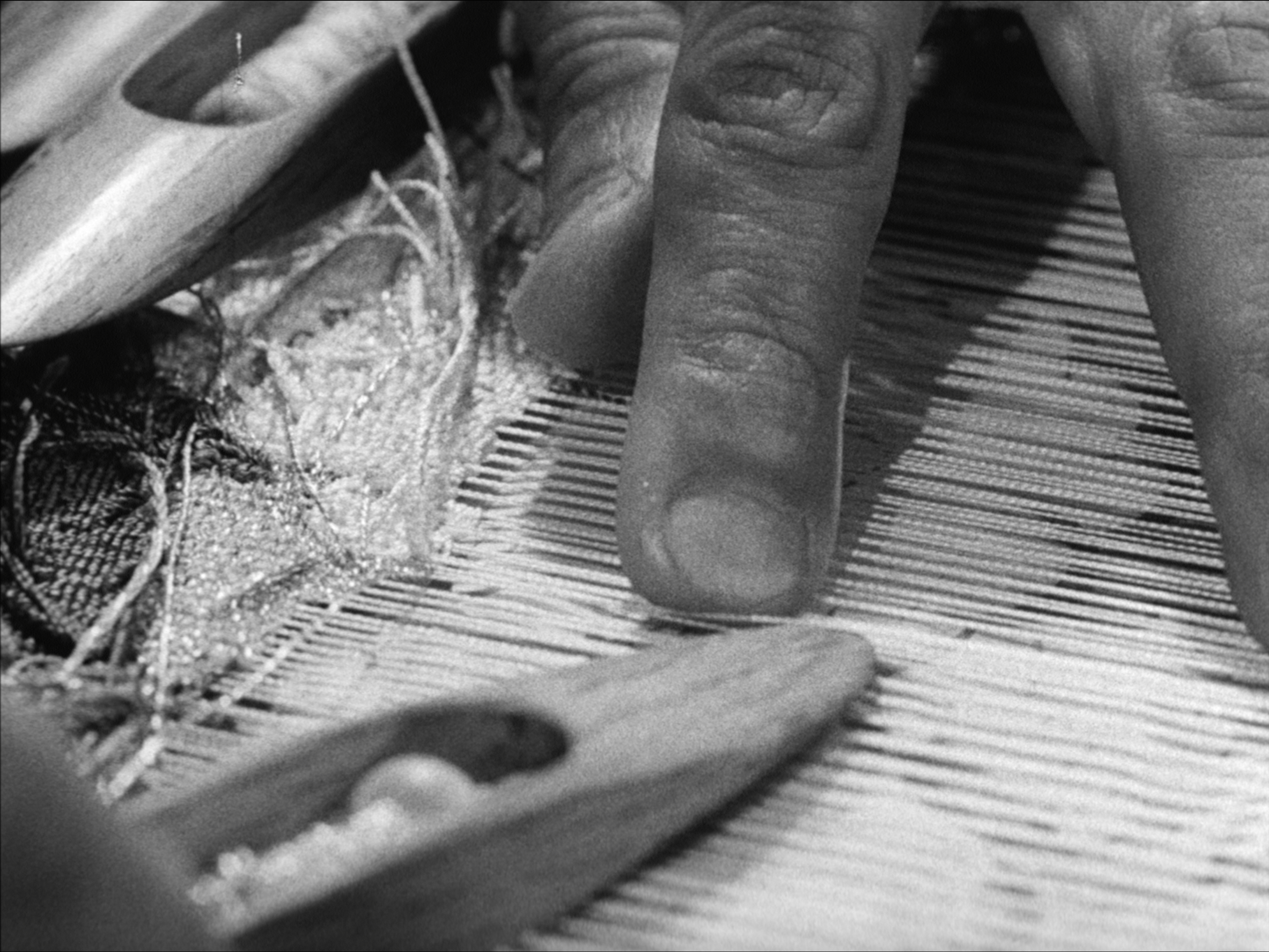Close-up of a weaver’s hand guiding threads across a traditional loom.