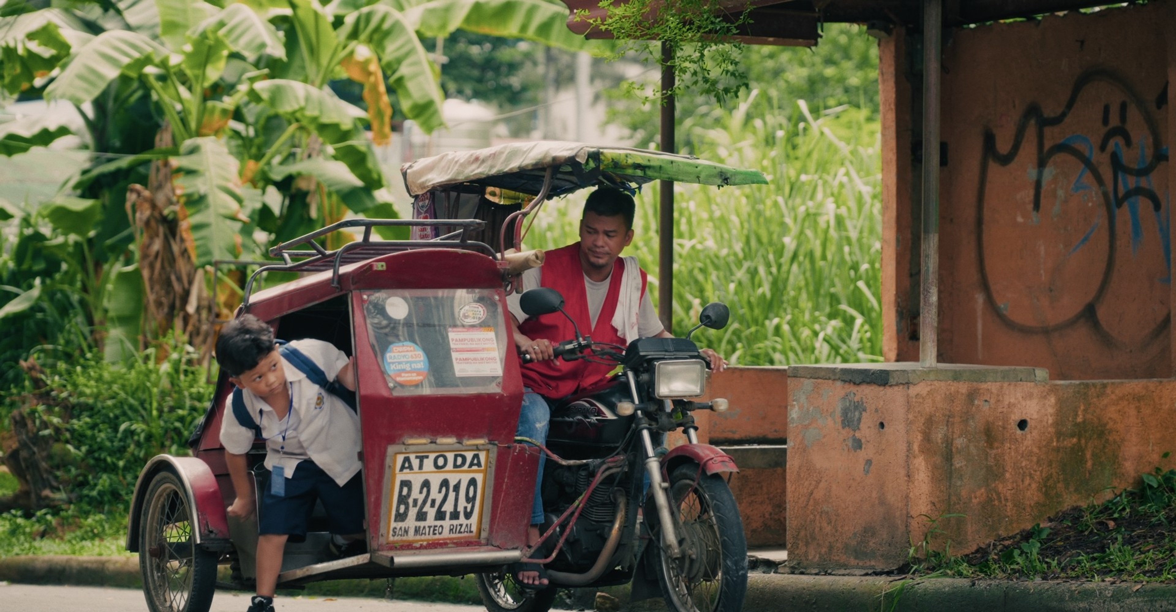 A young boy gets off a tricycle driven by a man.