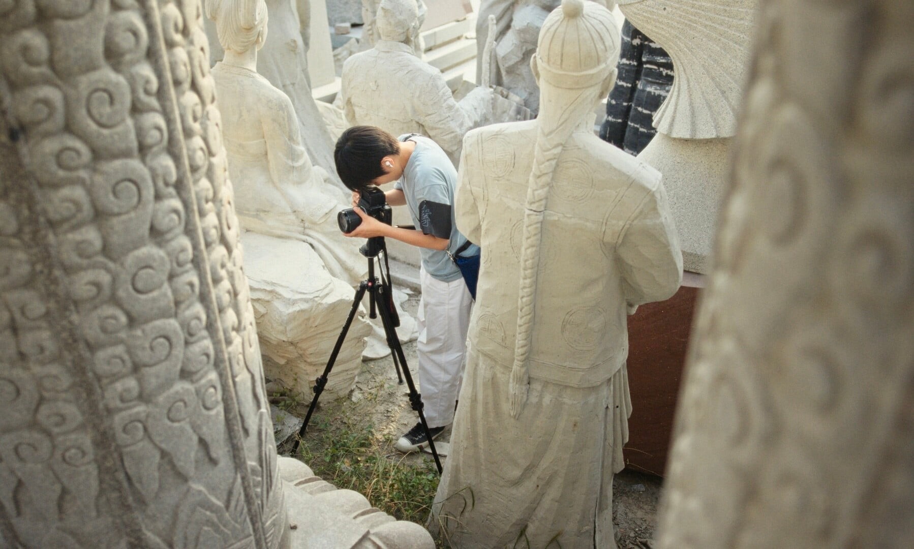 A person holds a camera in the midst of several white statues.