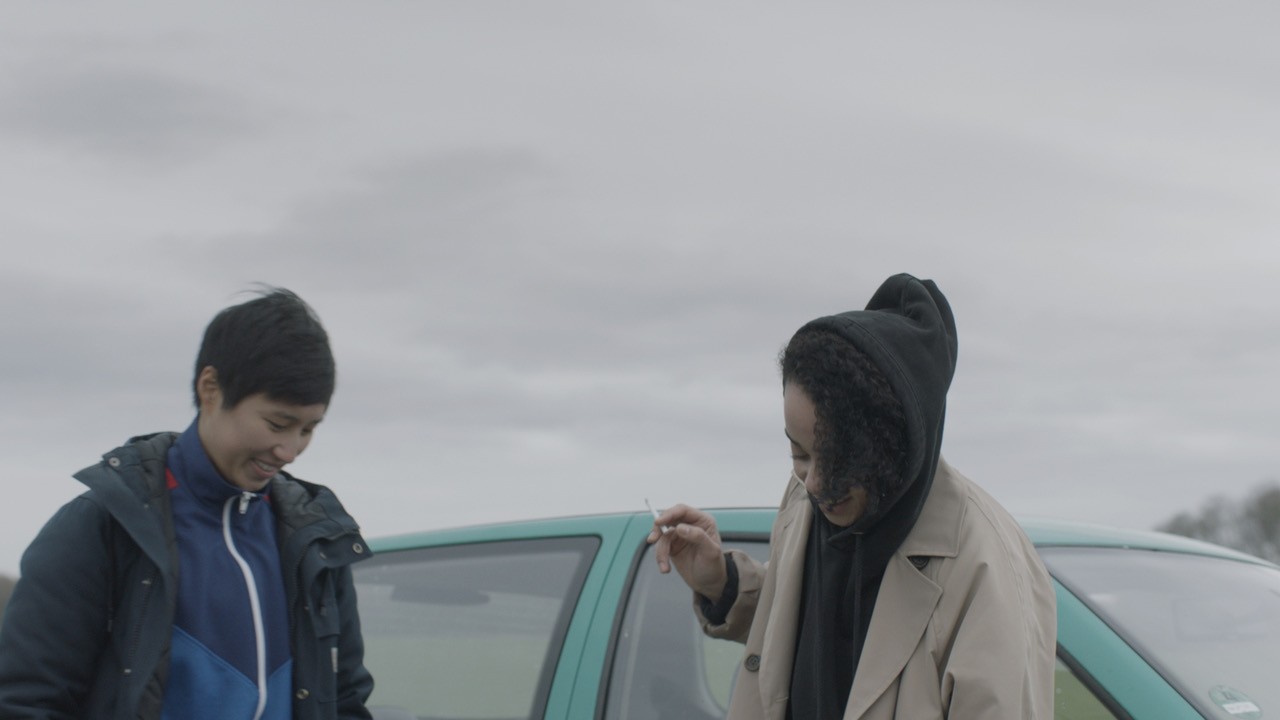 Two people standing beside a car on an overcast day, one holding up a set of keys.