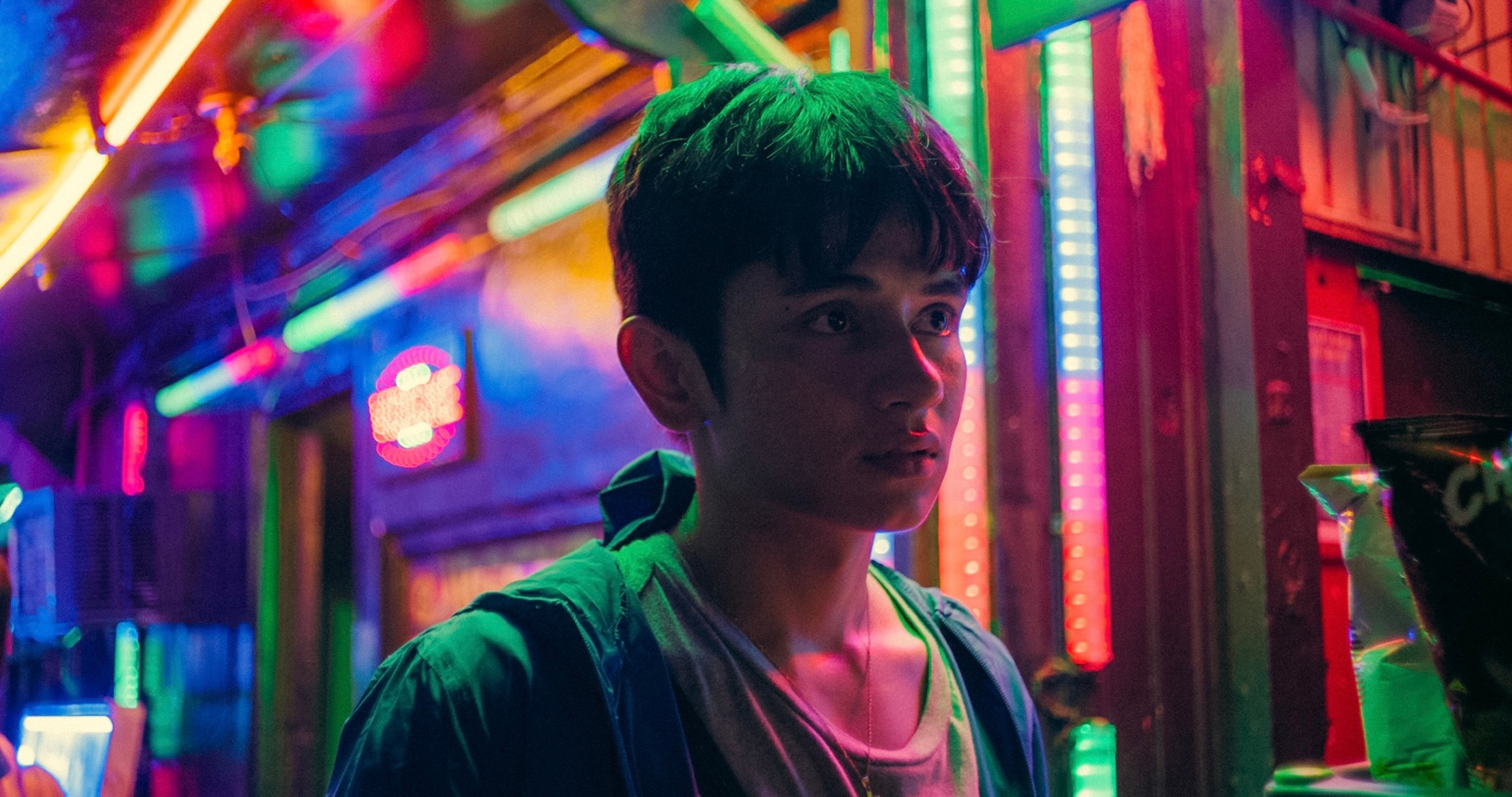 A young man standing on a street illuminated by vivid neon lights at night.