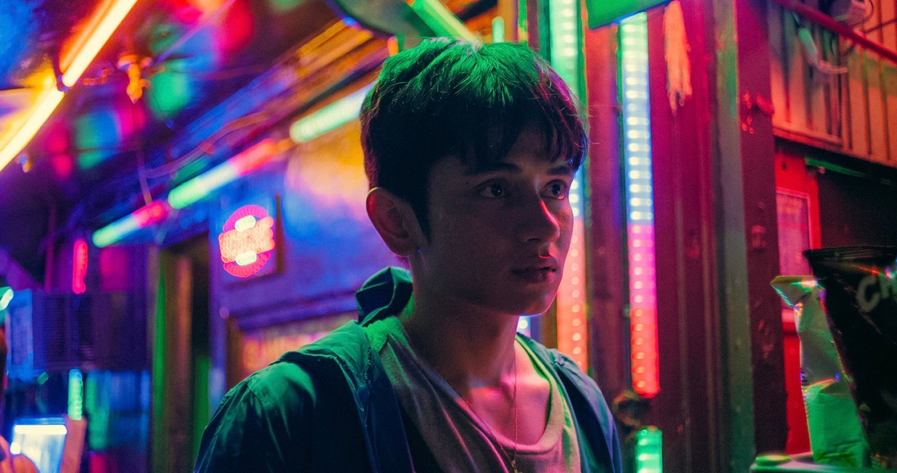 A young man standing on a street illuminated by vivid neon lights at night.