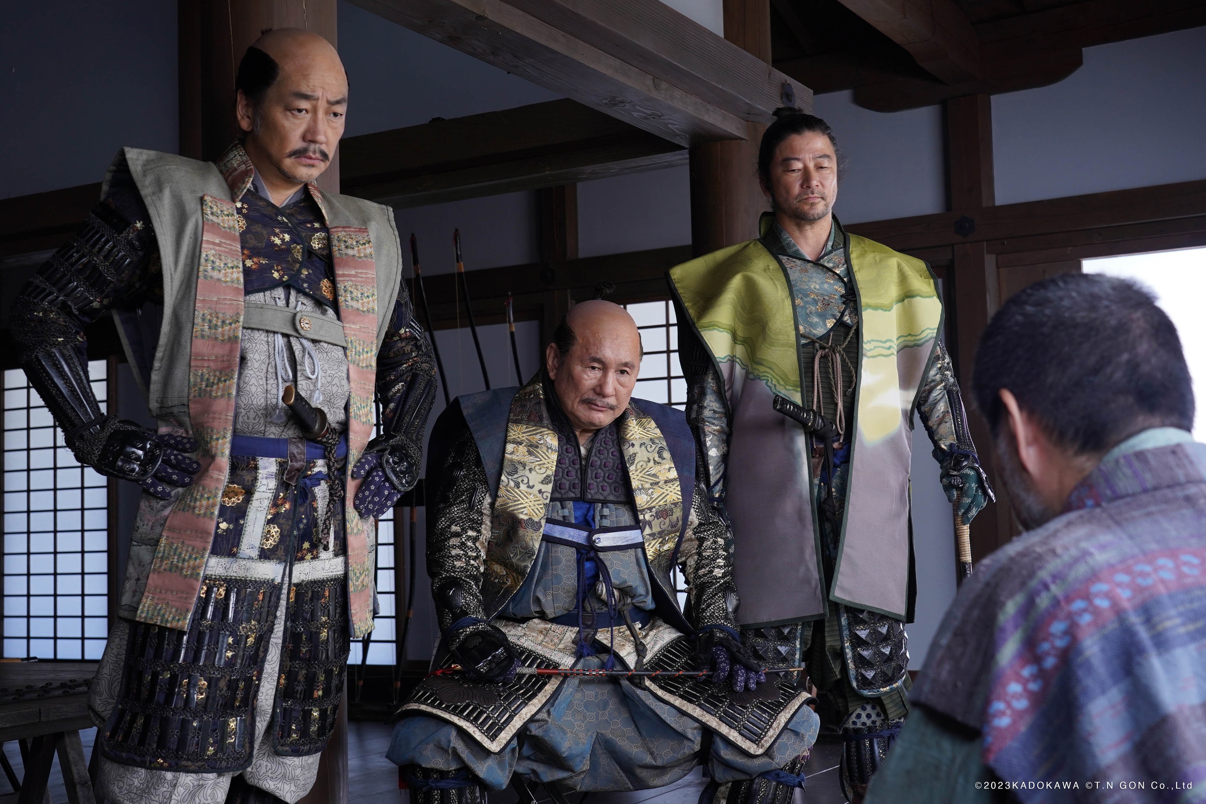 Three men in samurai armour standing before a seated man inside a traditional Japanese interior.