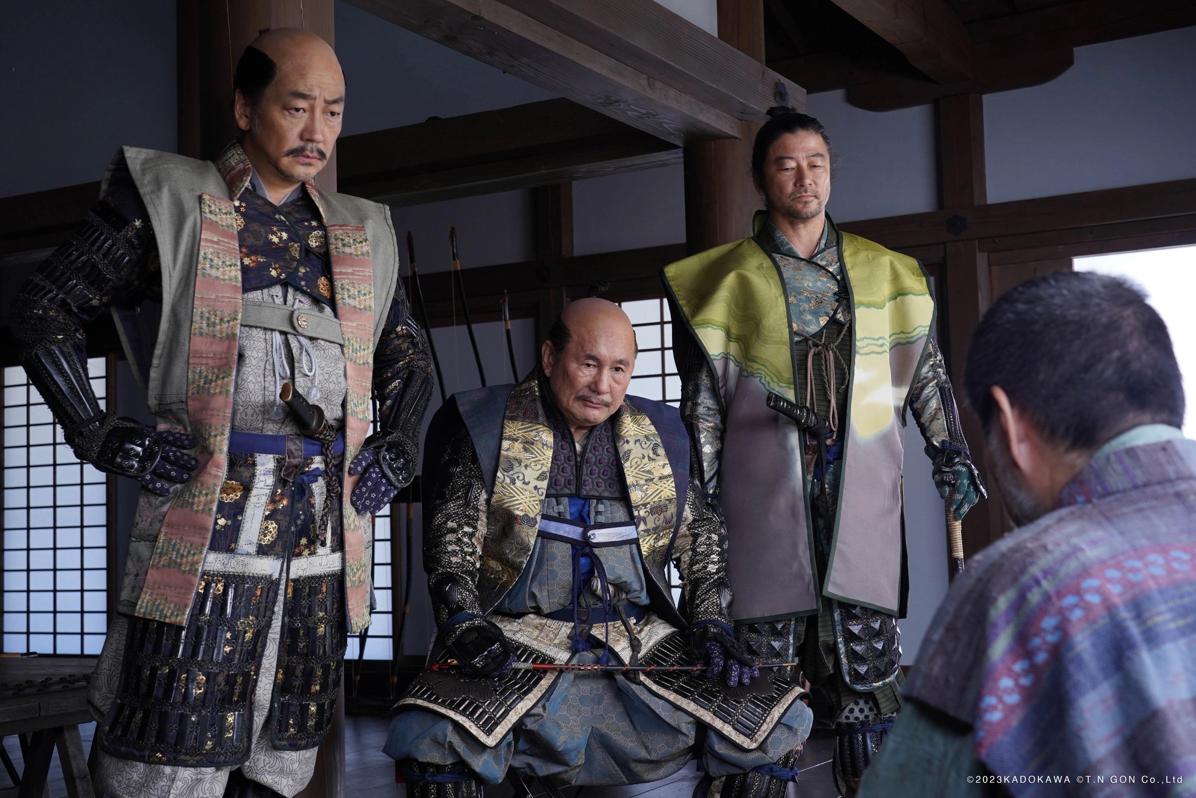 Three men in samurai armour standing before a seated man inside a traditional Japanese interior.