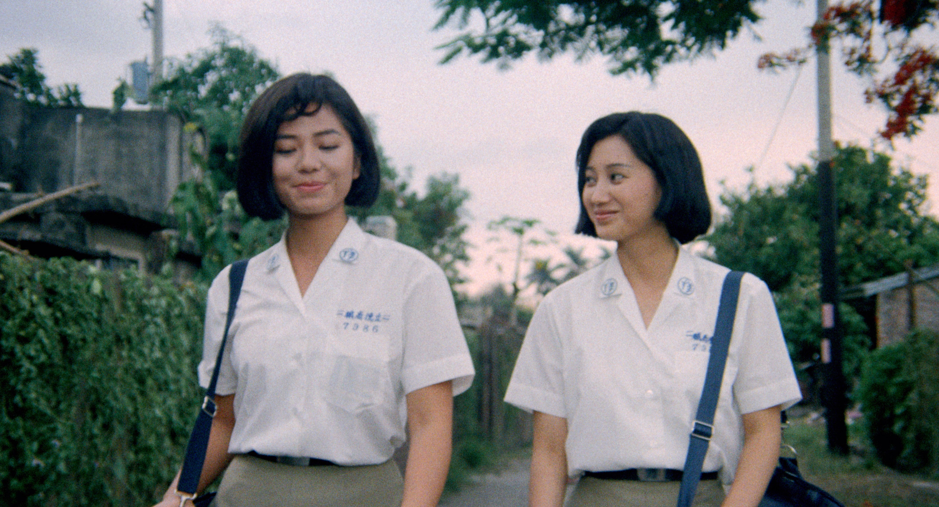 Two young women in matching school uniforms walking together along a quiet street.