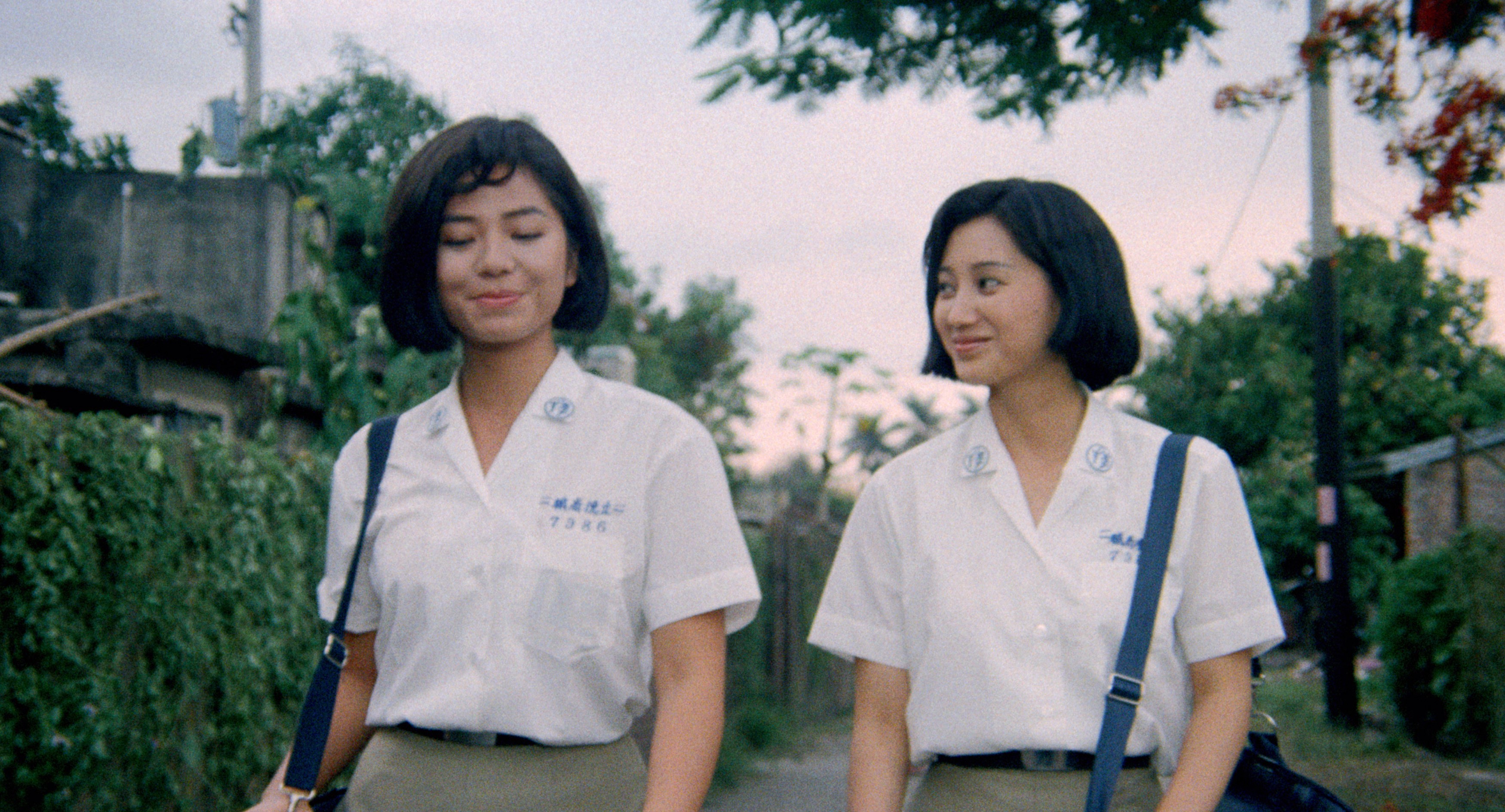 Two young women in matching school uniforms walking together along a quiet street.
