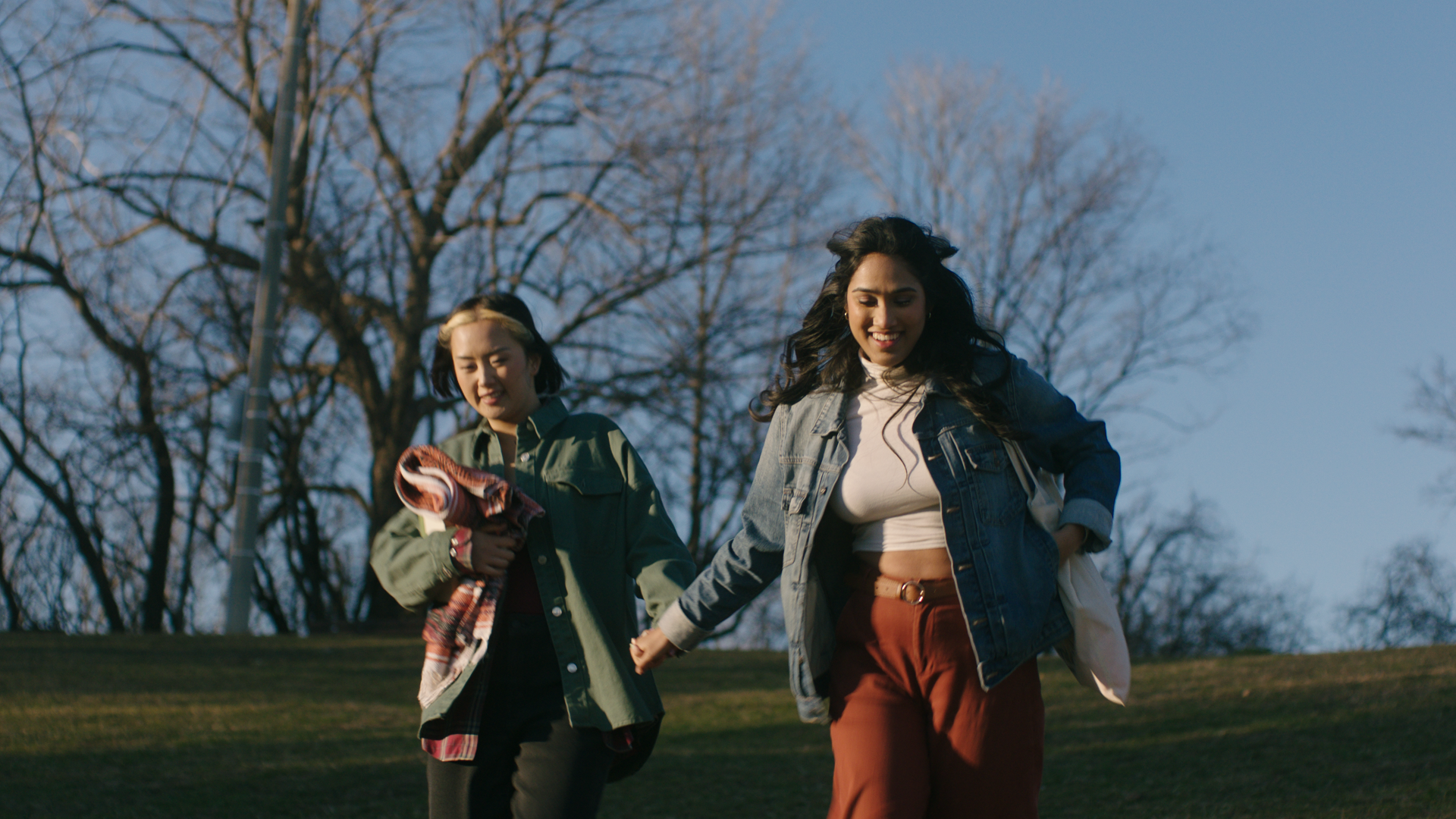 Two people holding hands as they walk together through a park on a clear day.