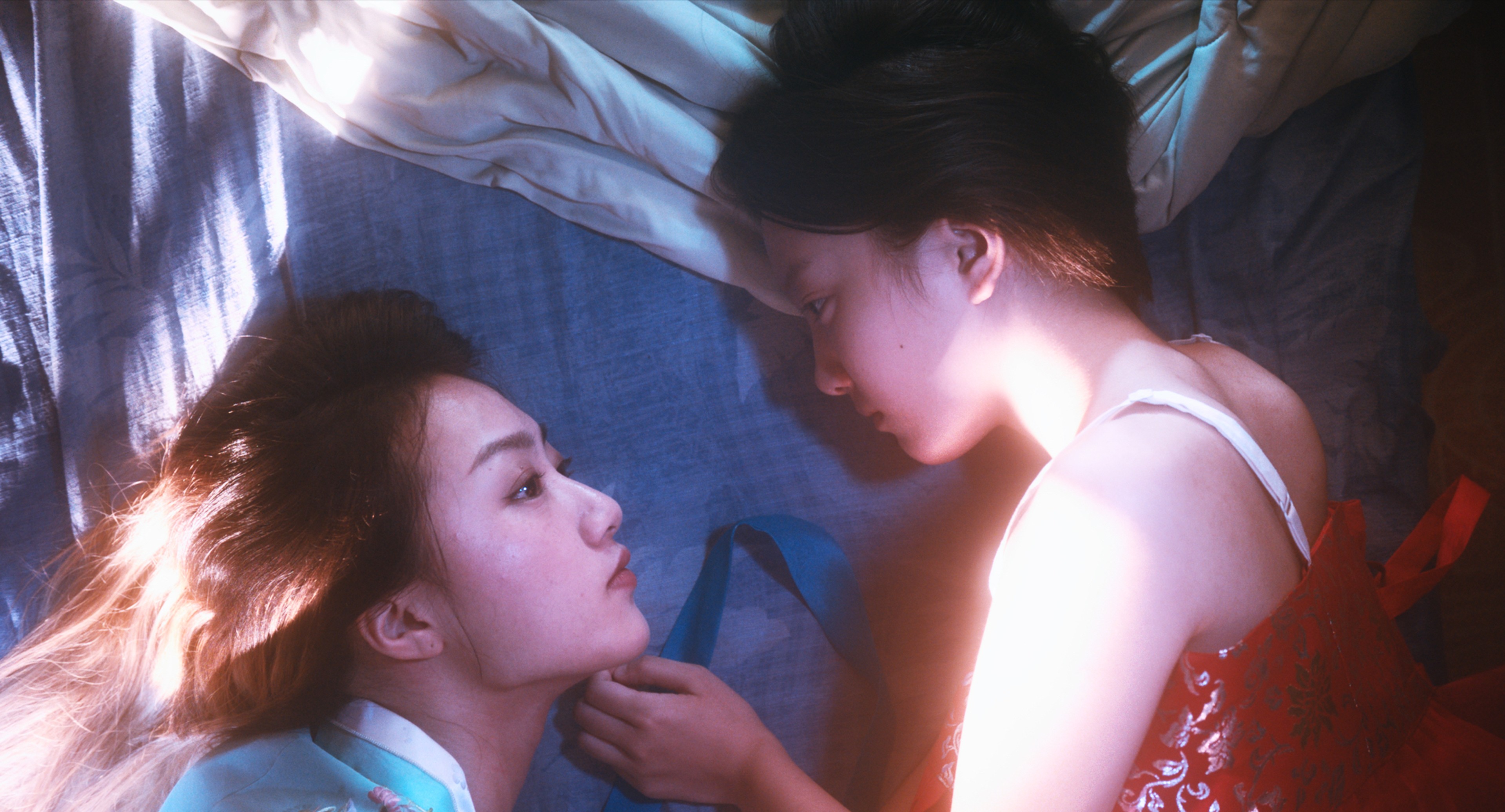 Two women lying close together, gazing at each other in soft light.