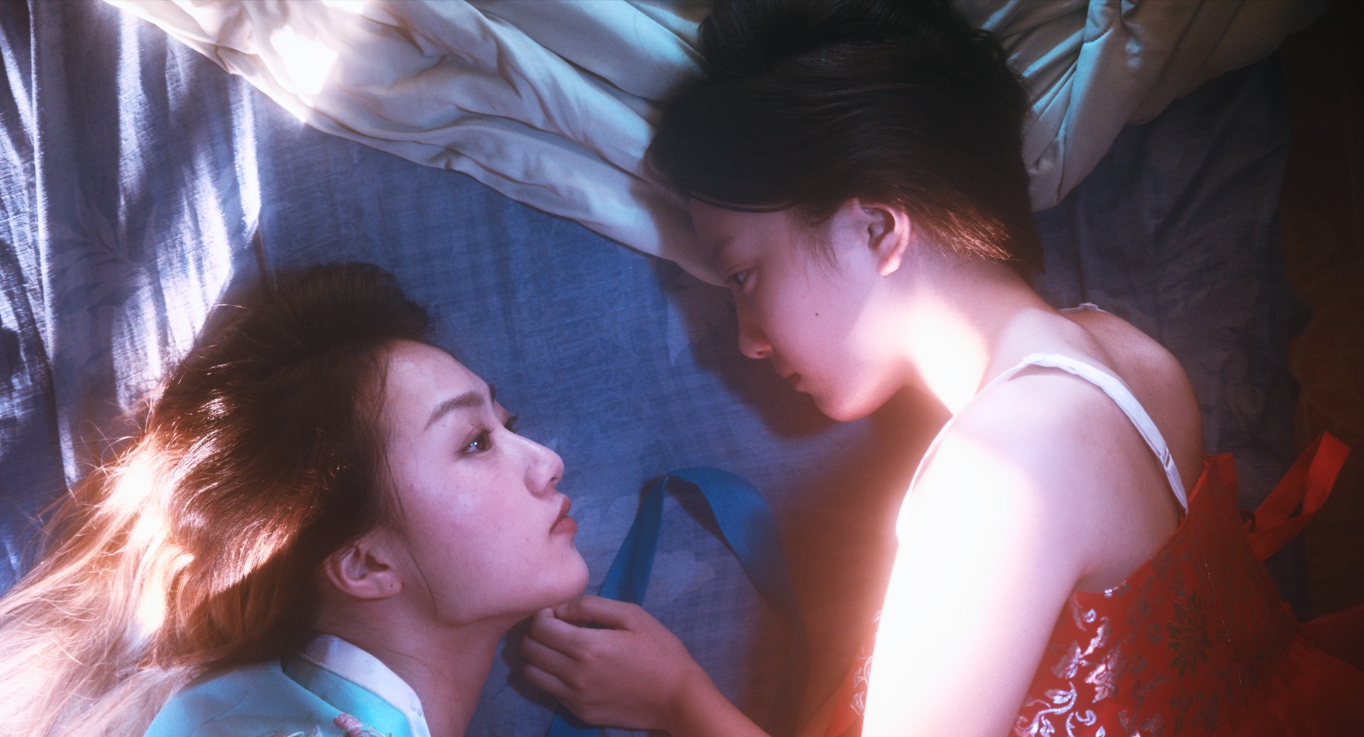 Two women lying close together, gazing at each other in soft light.