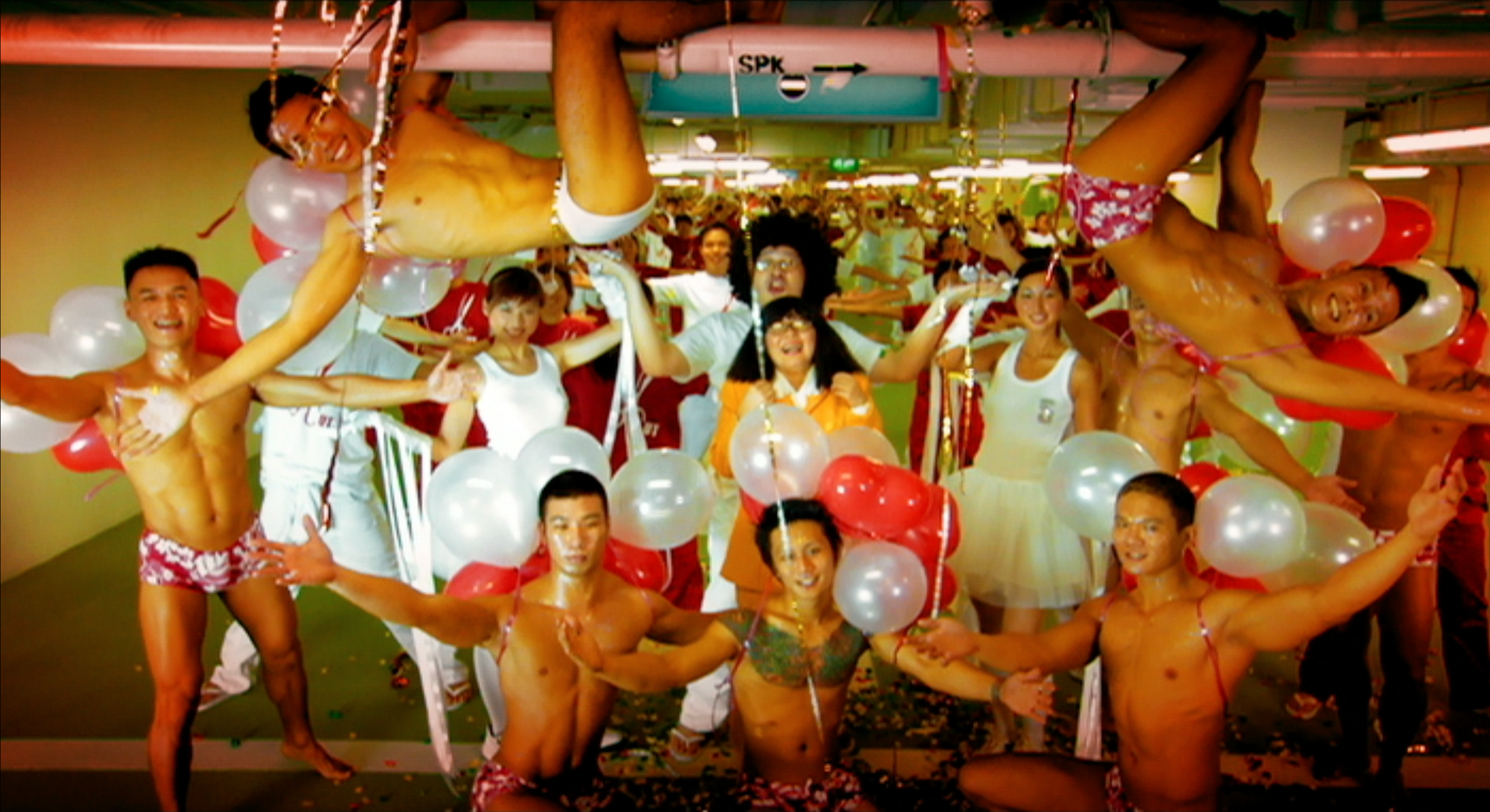 A celebratory group posing with balloons, surrounded by shirtless performers in matching patterned briefs.