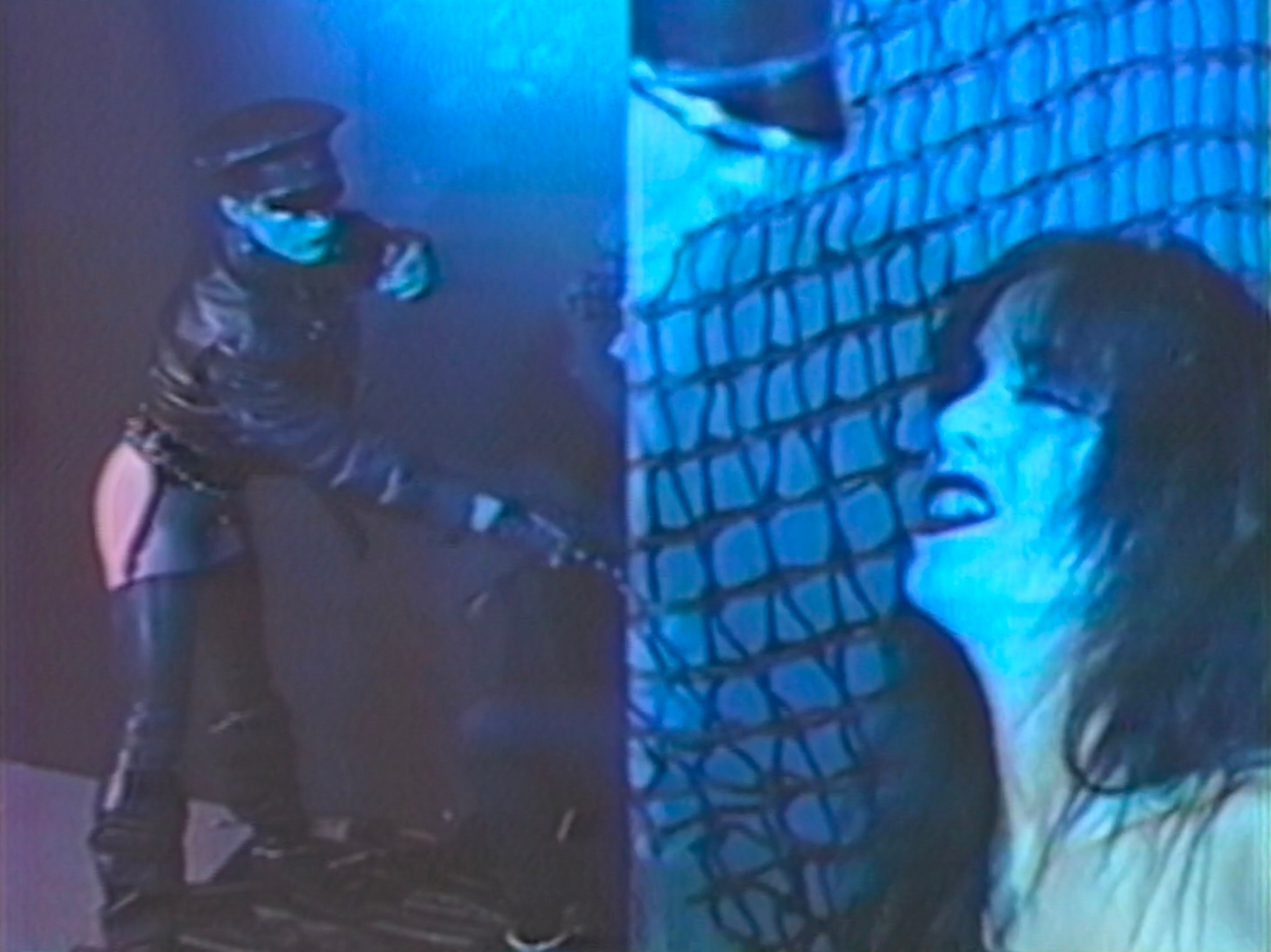 A leather-clad dominatrix whips a woman.
