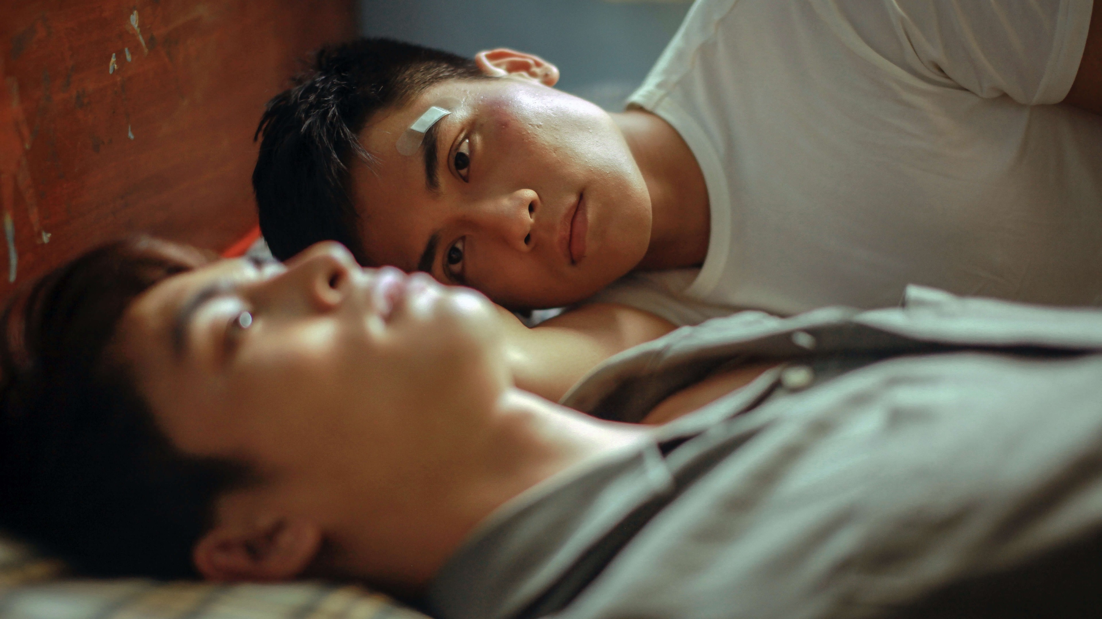 Two men lying side by side in bed.