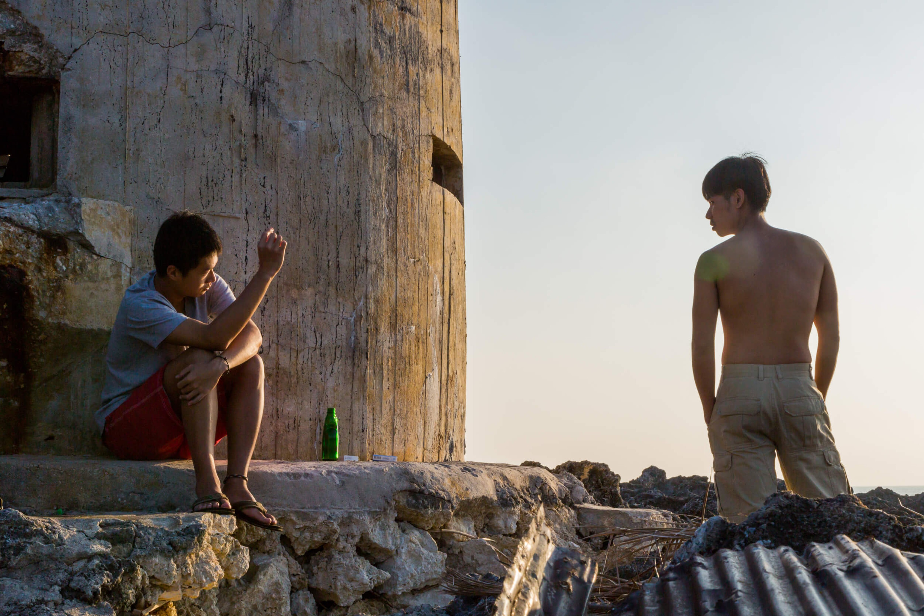 A man sitting on a stone slab looks at a man standing a few feet away.