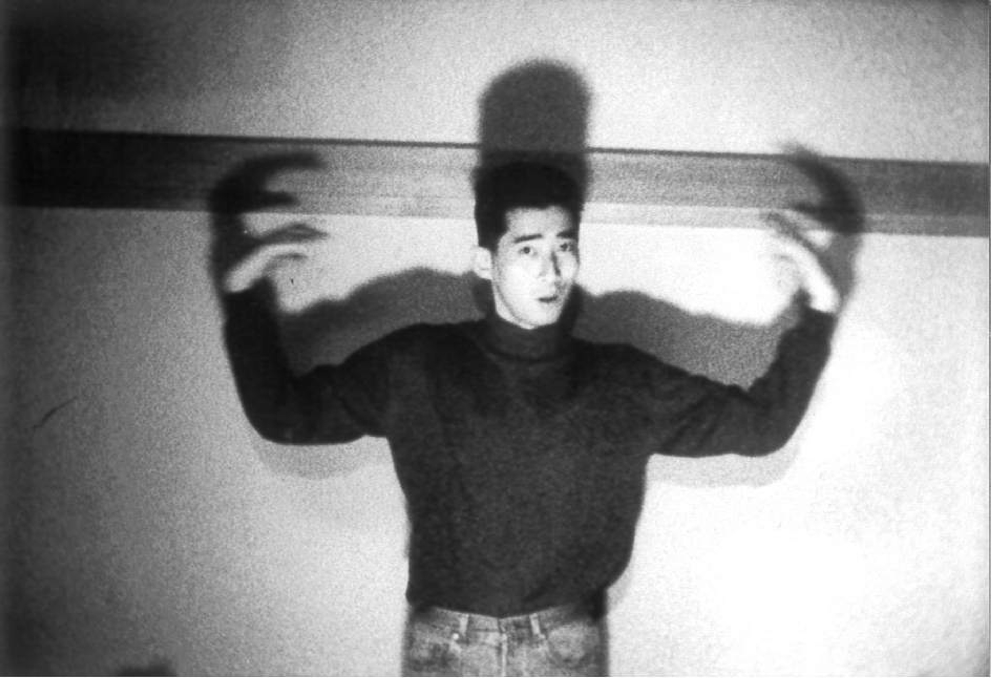 A man stands with his arms up, casting a shadow on the wall behind him.