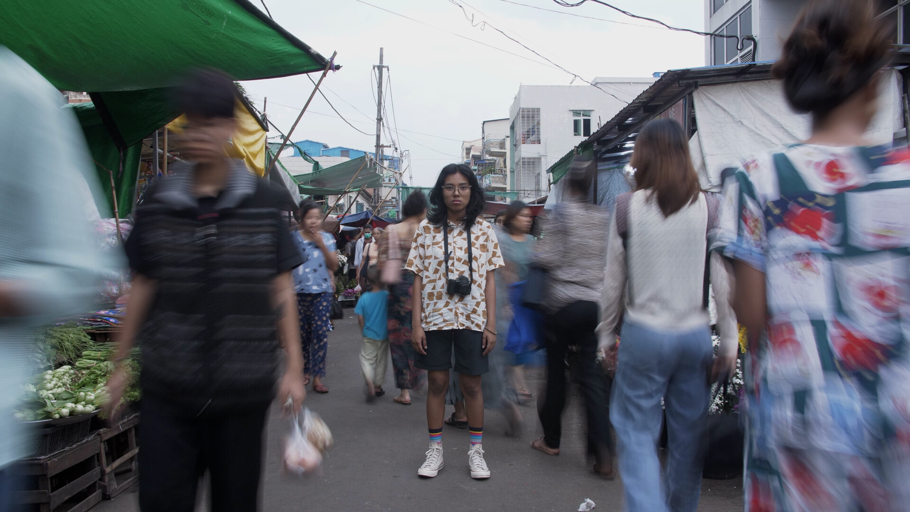 a person with a camera stands in the middle of a busy market.