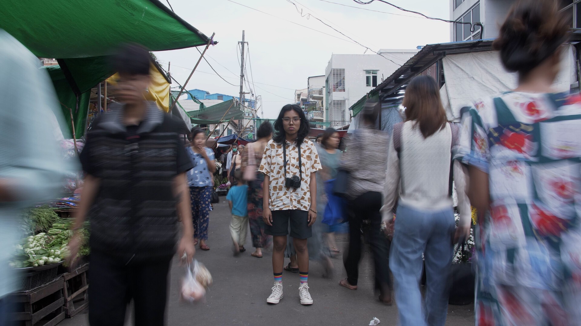 a person with a camera stands in the middle of a busy market.