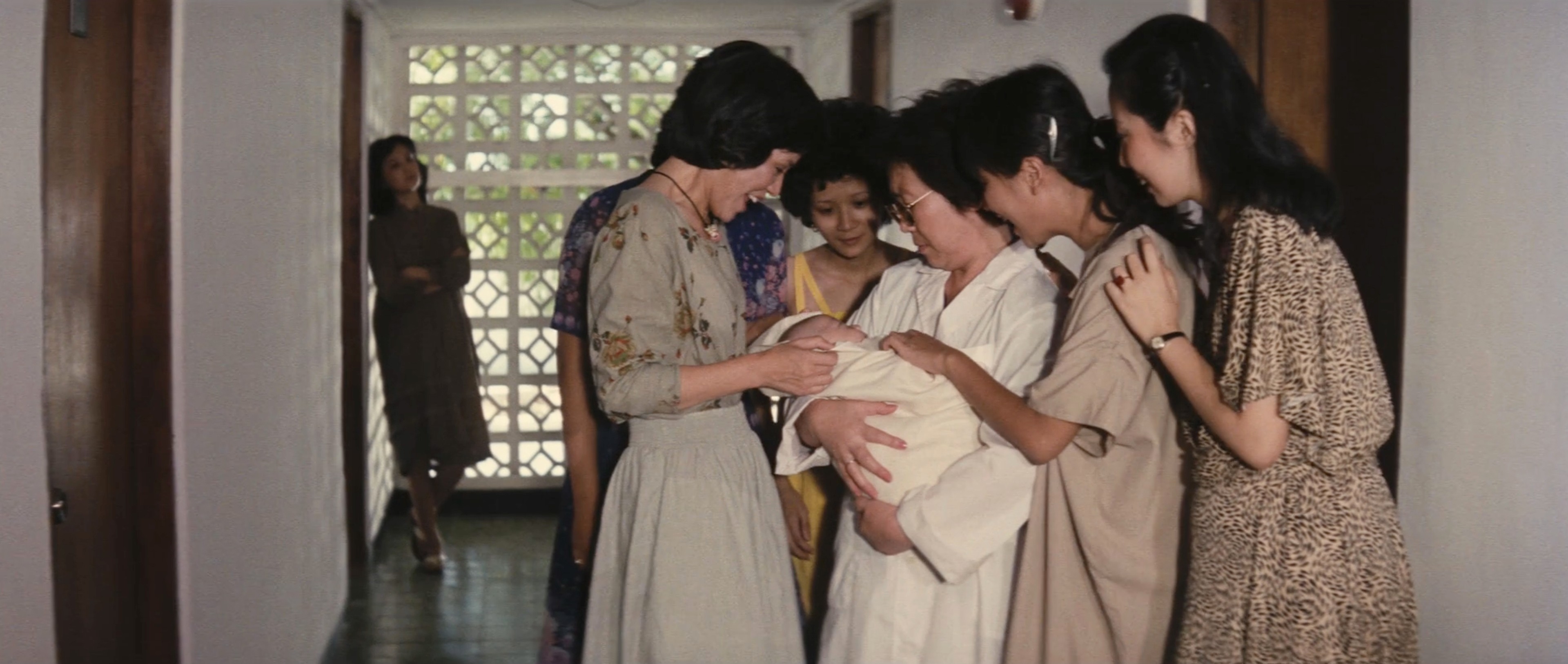 A group of women gathered closely around a swaddled baby in a hallway.