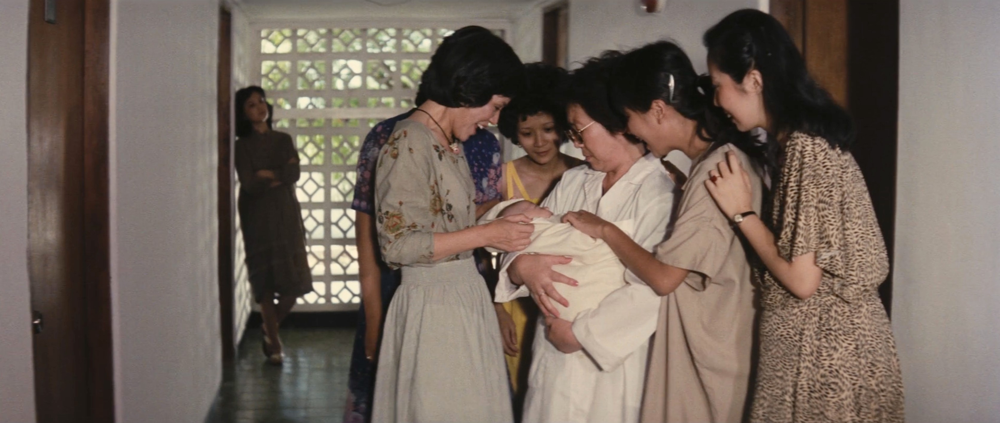 A group of women gathered closely around a swaddled baby in a hallway.