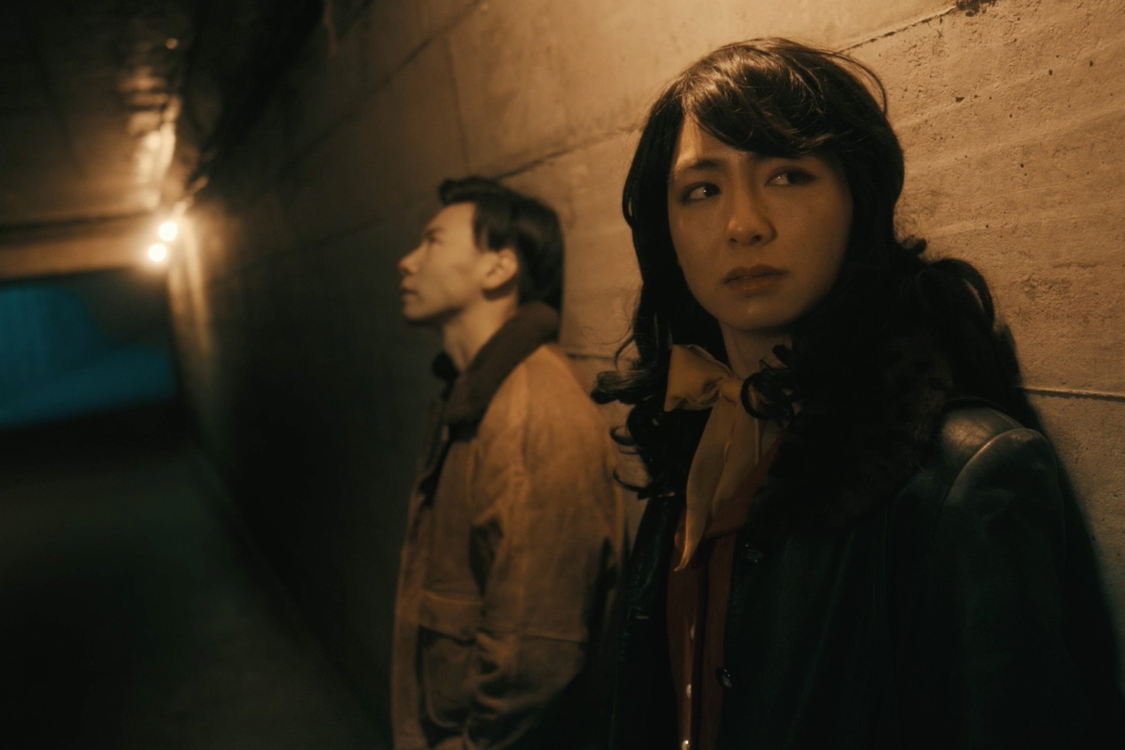 Two figures leaning against a wall in a dimly lit alley.
