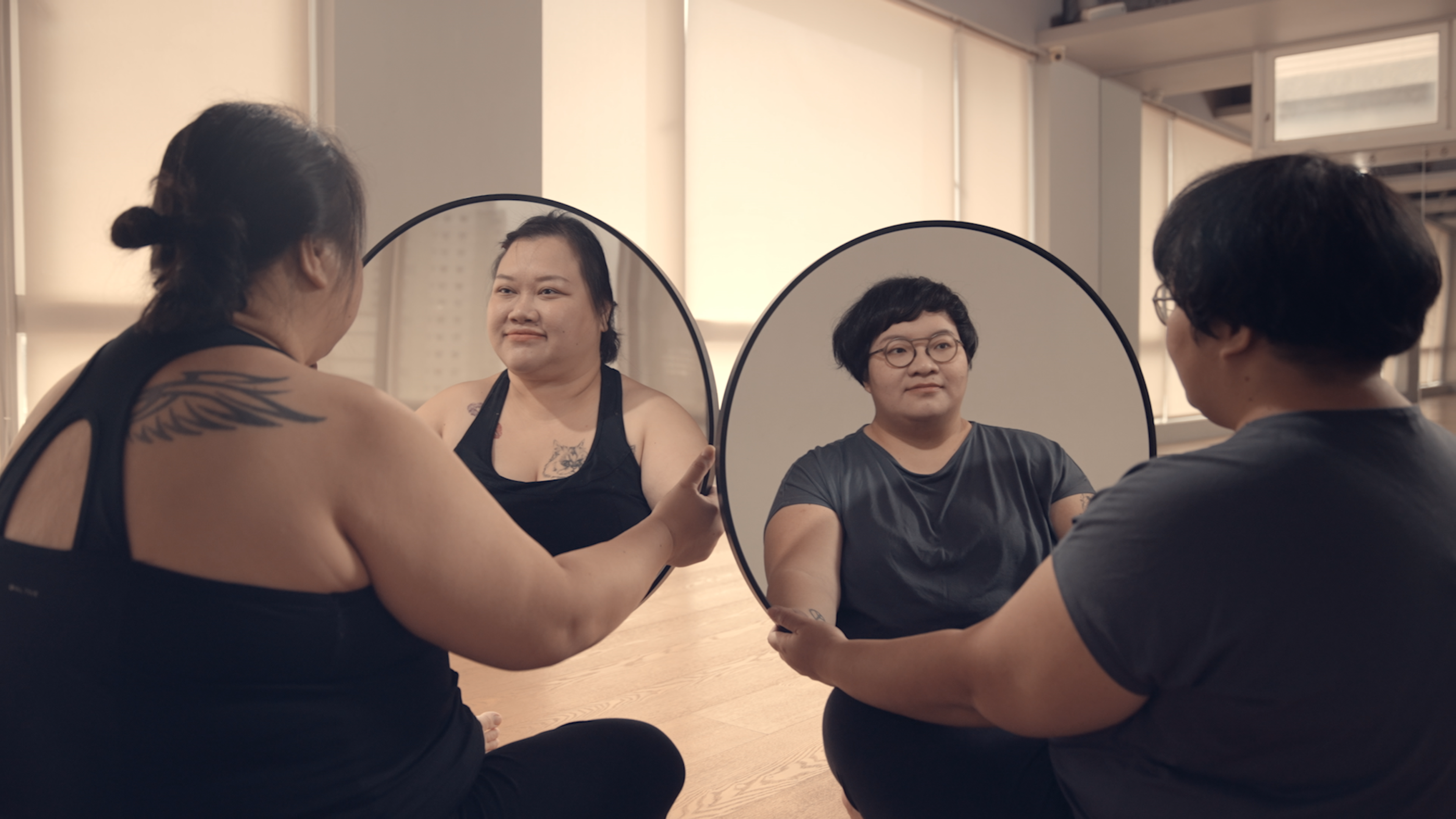 Two women each hold up a round mirror and look at their own reflections.