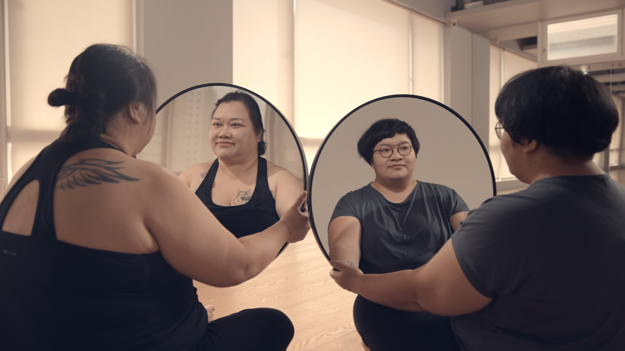 Two women each hold up a round mirror and look at their own reflections.