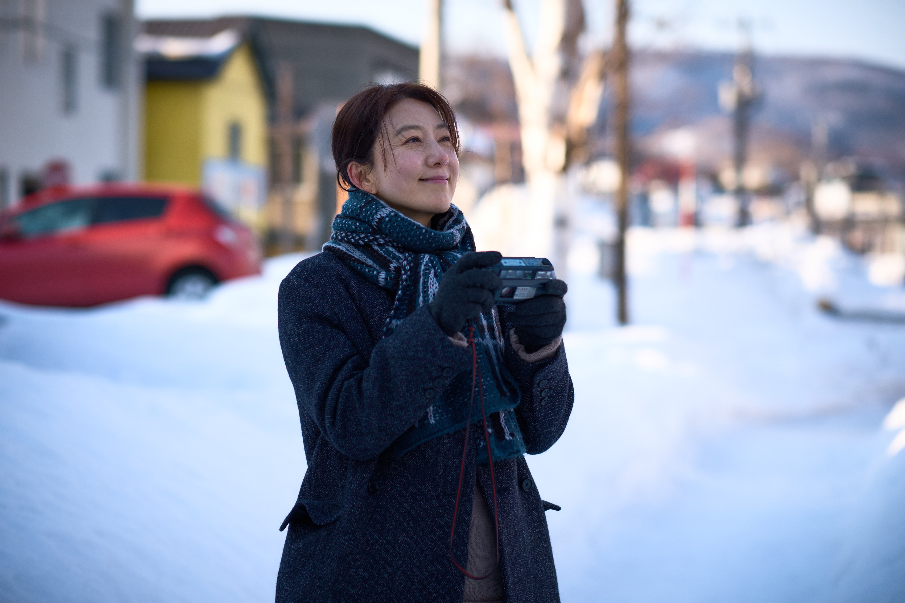 A woman smiling and holding a camera against the backdrop of snow.