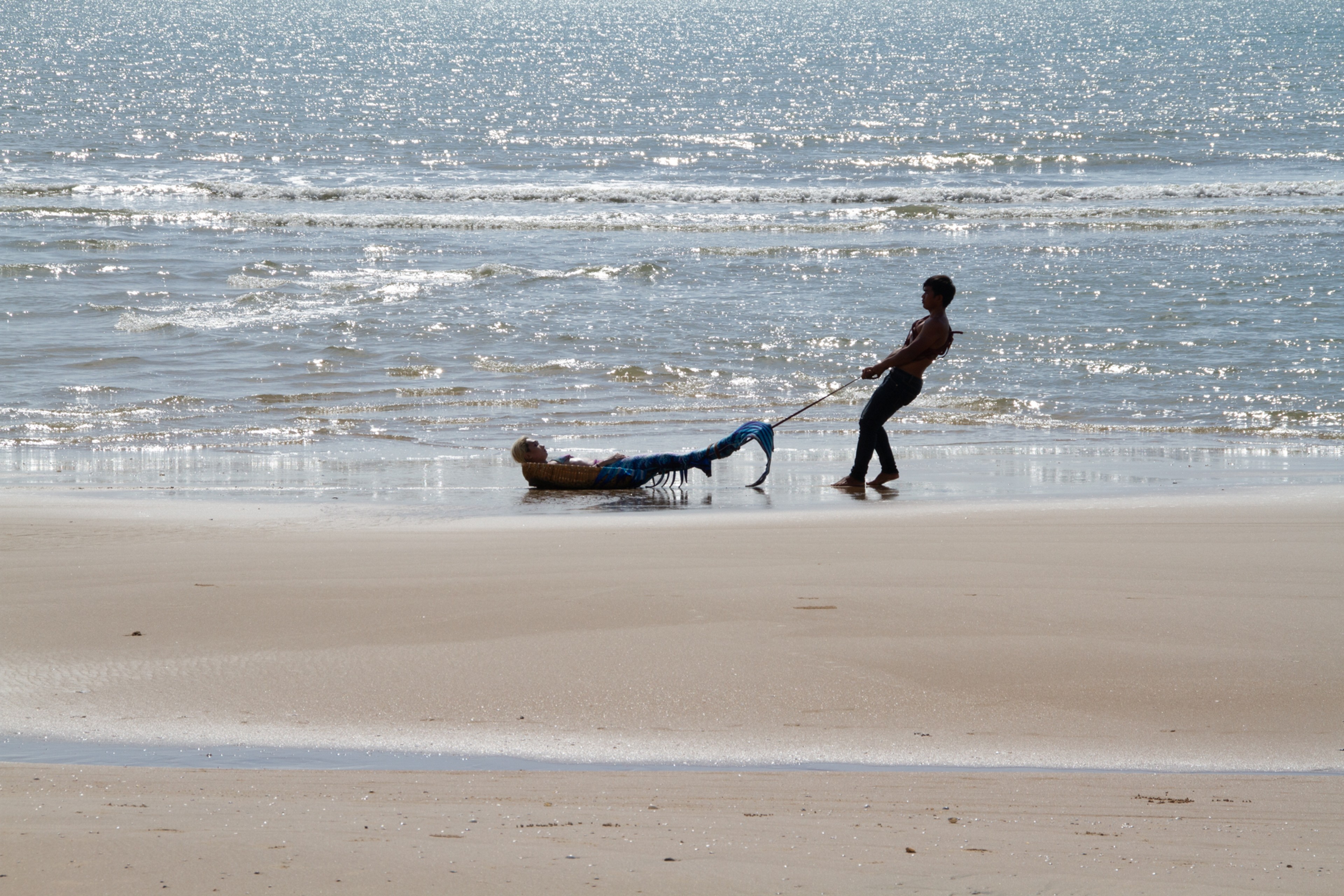 A person drags a mermaid across a beach.