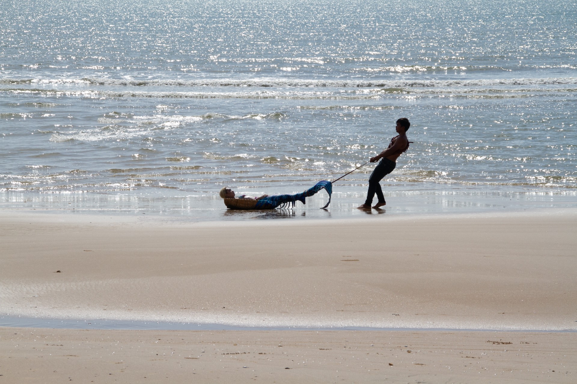 A person drags a mermaid across a beach.
