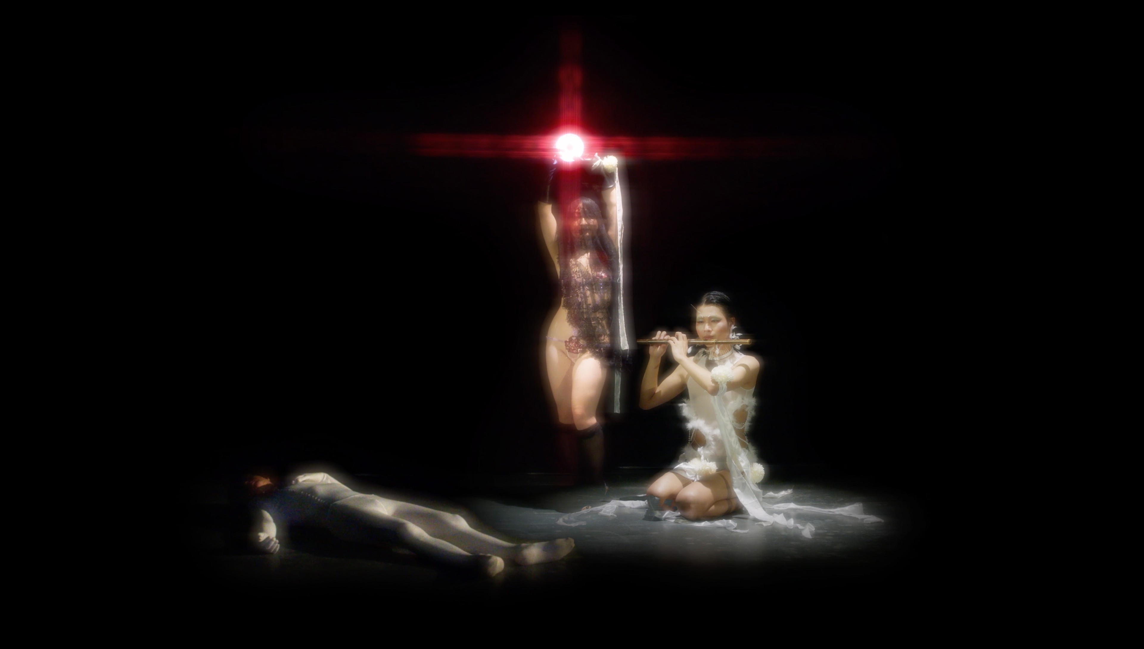 A tableau of three figures: one playing the flute; another holding up a red light; the other lying on the floor.