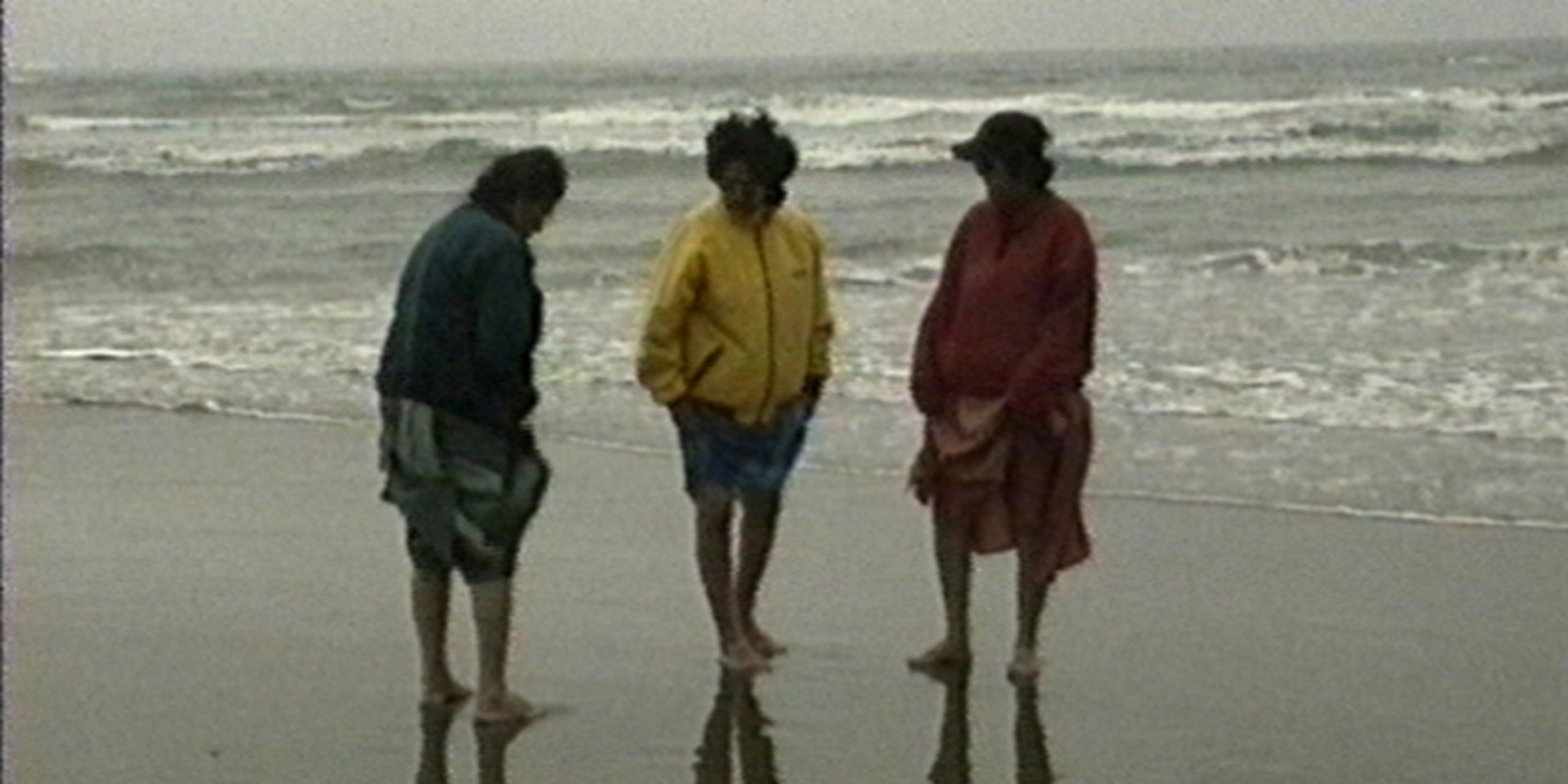 Three figures stand on a beach.