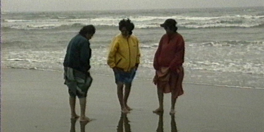 Three figures stand on a beach.