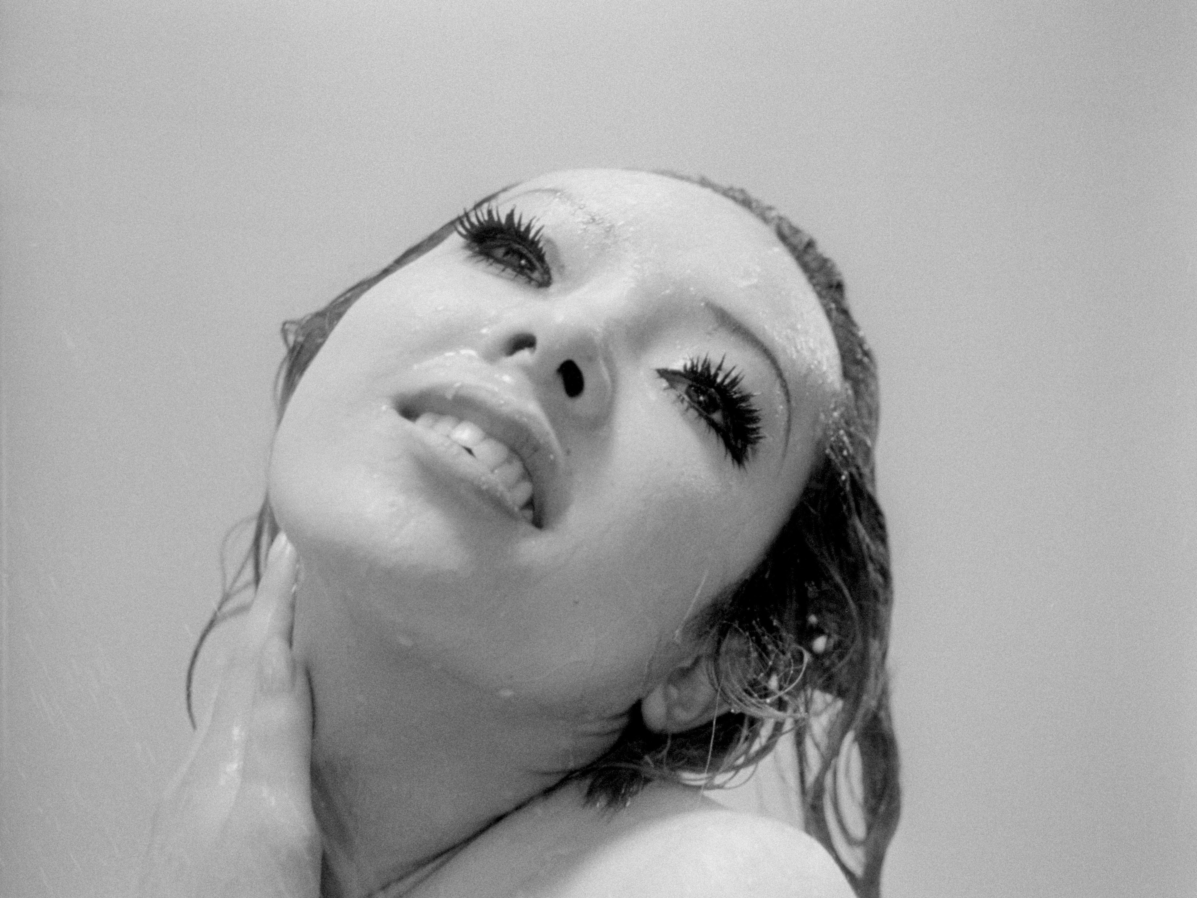 A person's face with thick eyelashes and wet hair smiling.