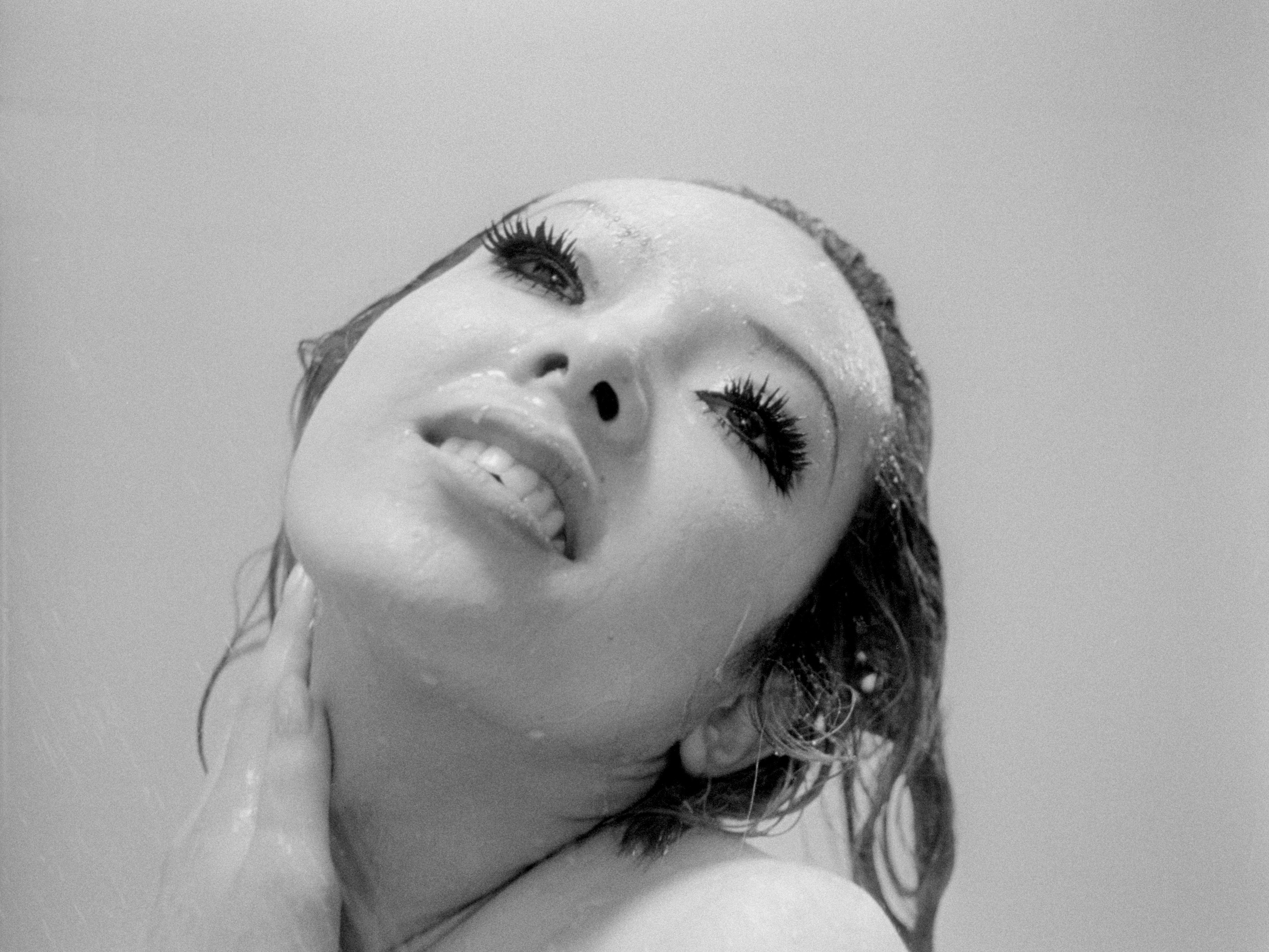 A person's face with thick eyelashes and wet hair smiling.