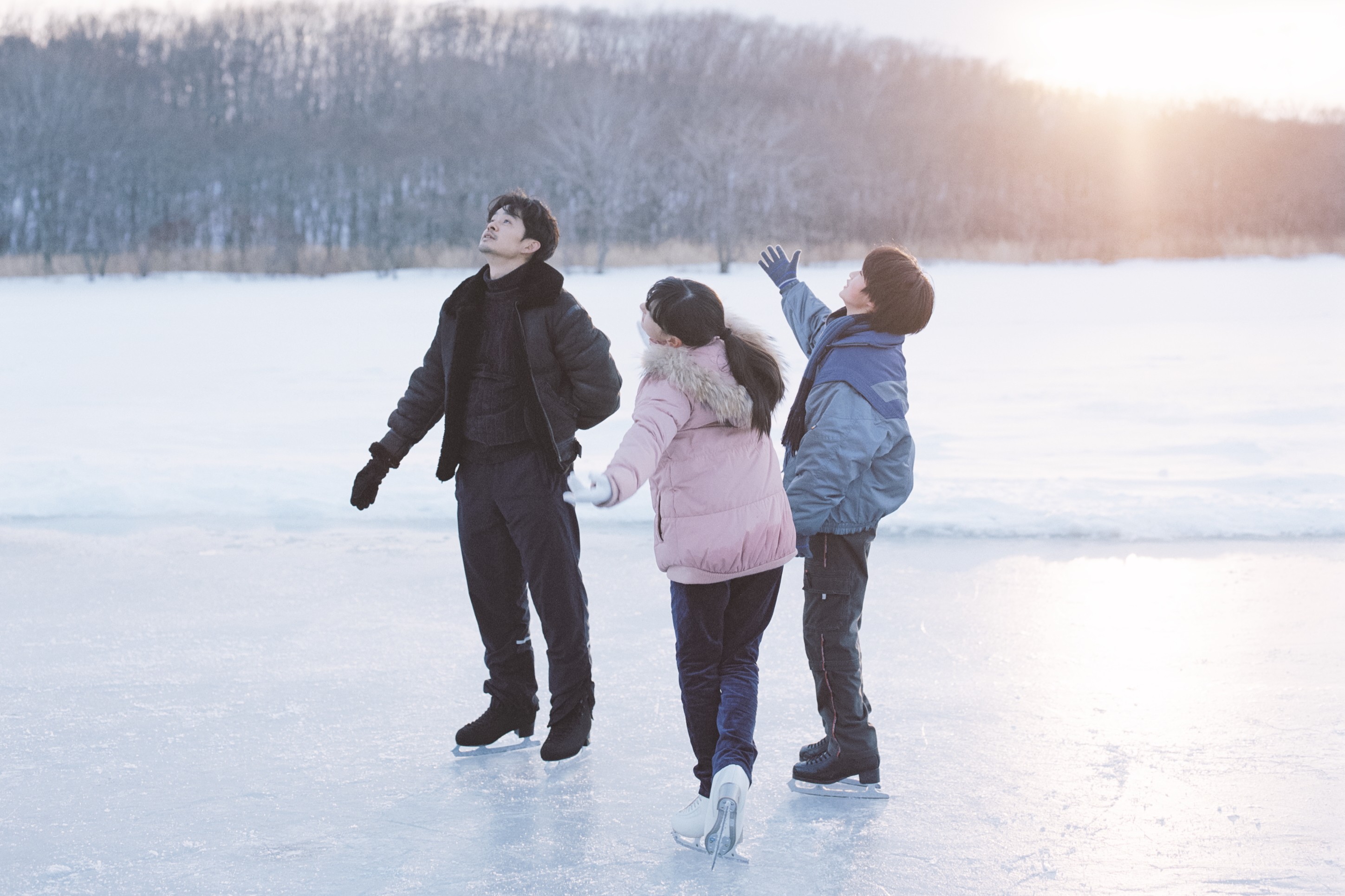 Three people in winter clothing standing together on a frozen lake at sunset.