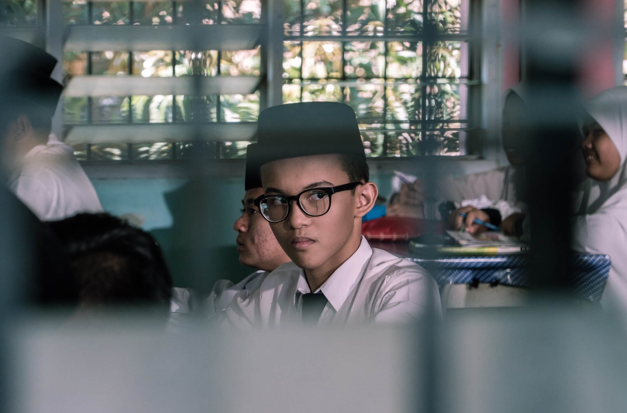 A boy in a classroom framed through blinds.