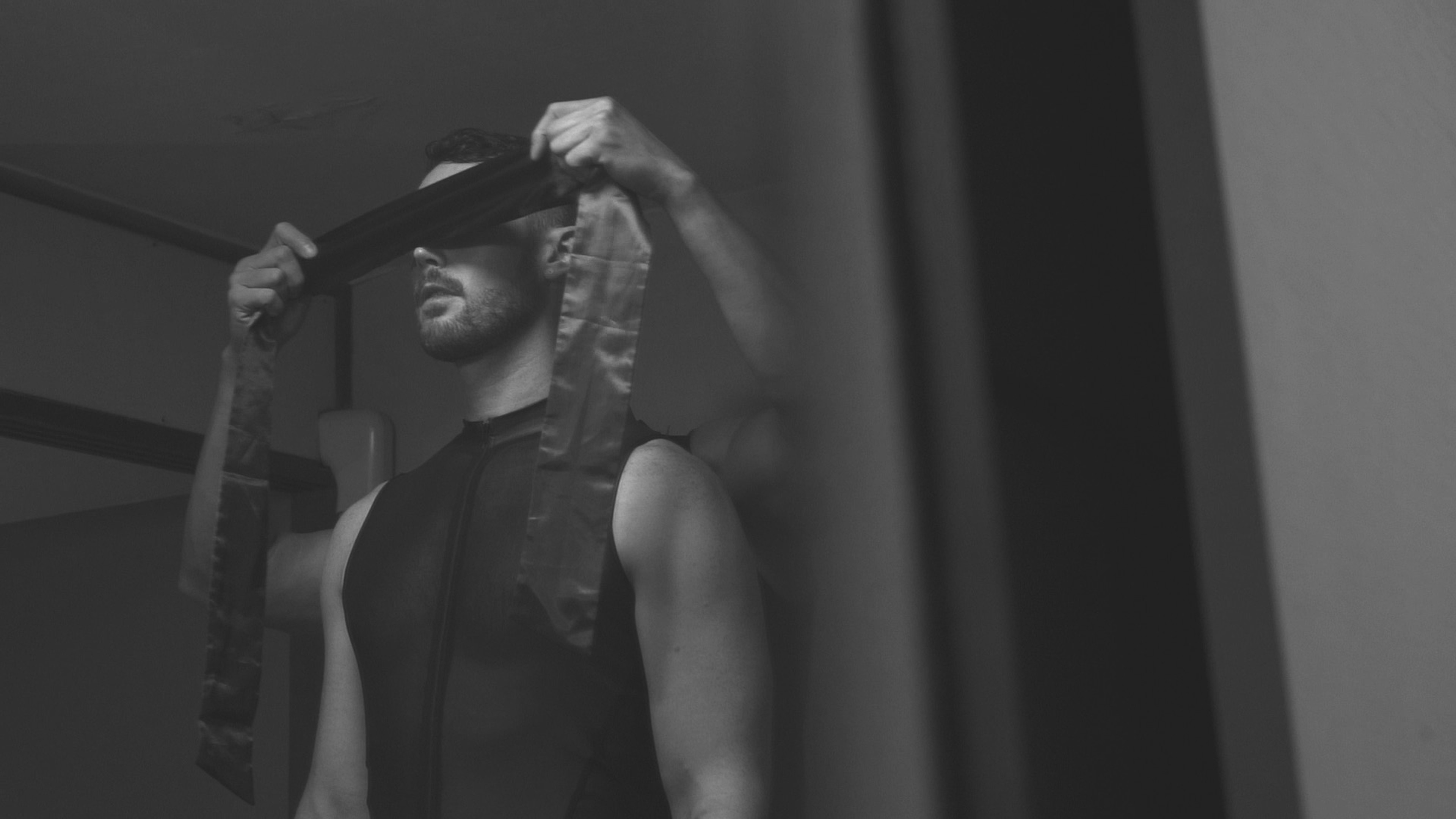 A person being blindfolded with a long strip of fabric in a black-and-white scene.