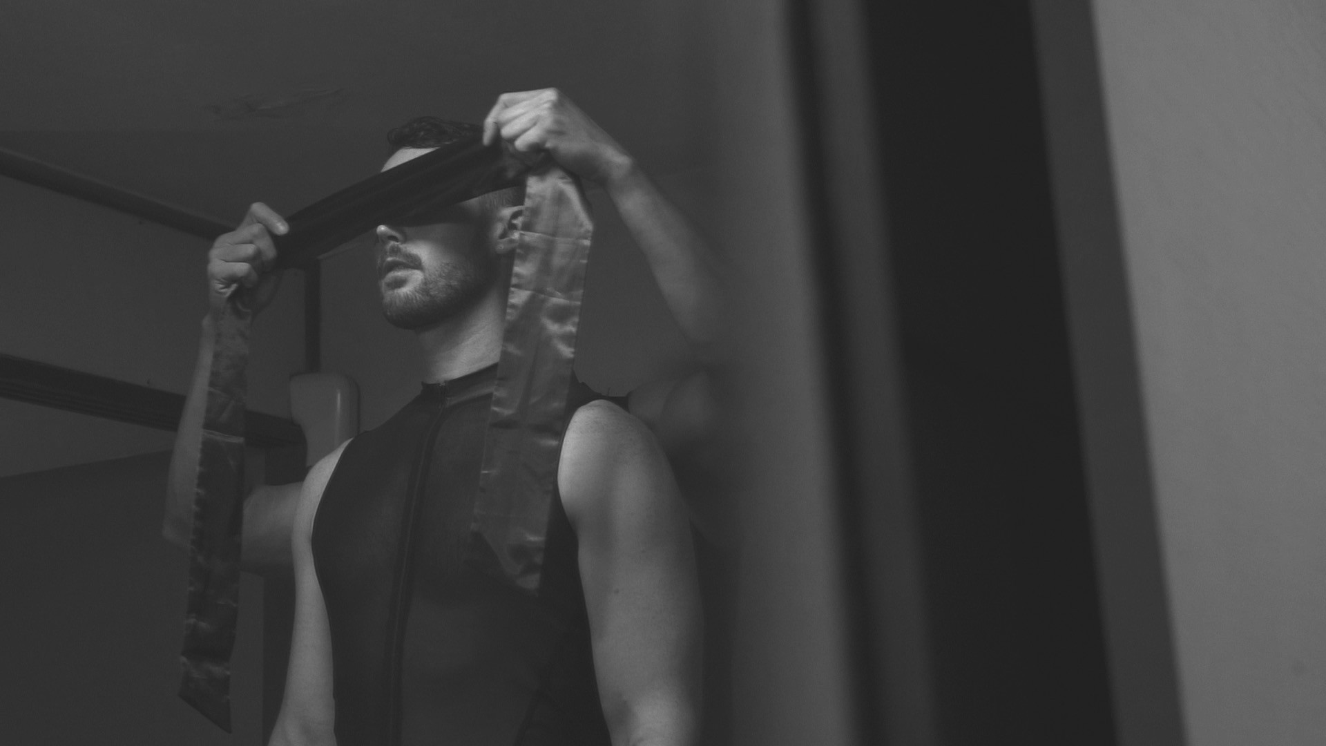 A person being blindfolded with a long strip of fabric in a black-and-white scene.