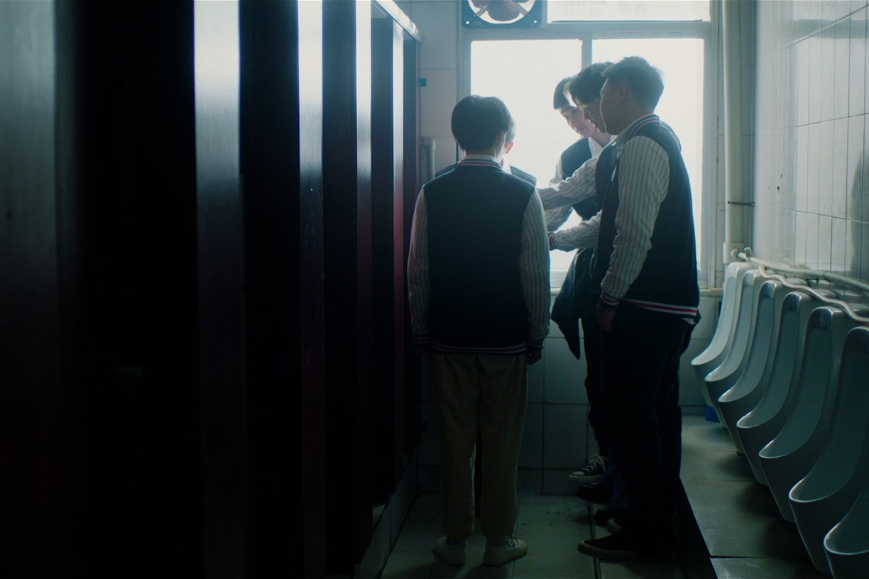 A group of young men gathered in a public restroom near a row of urinals.