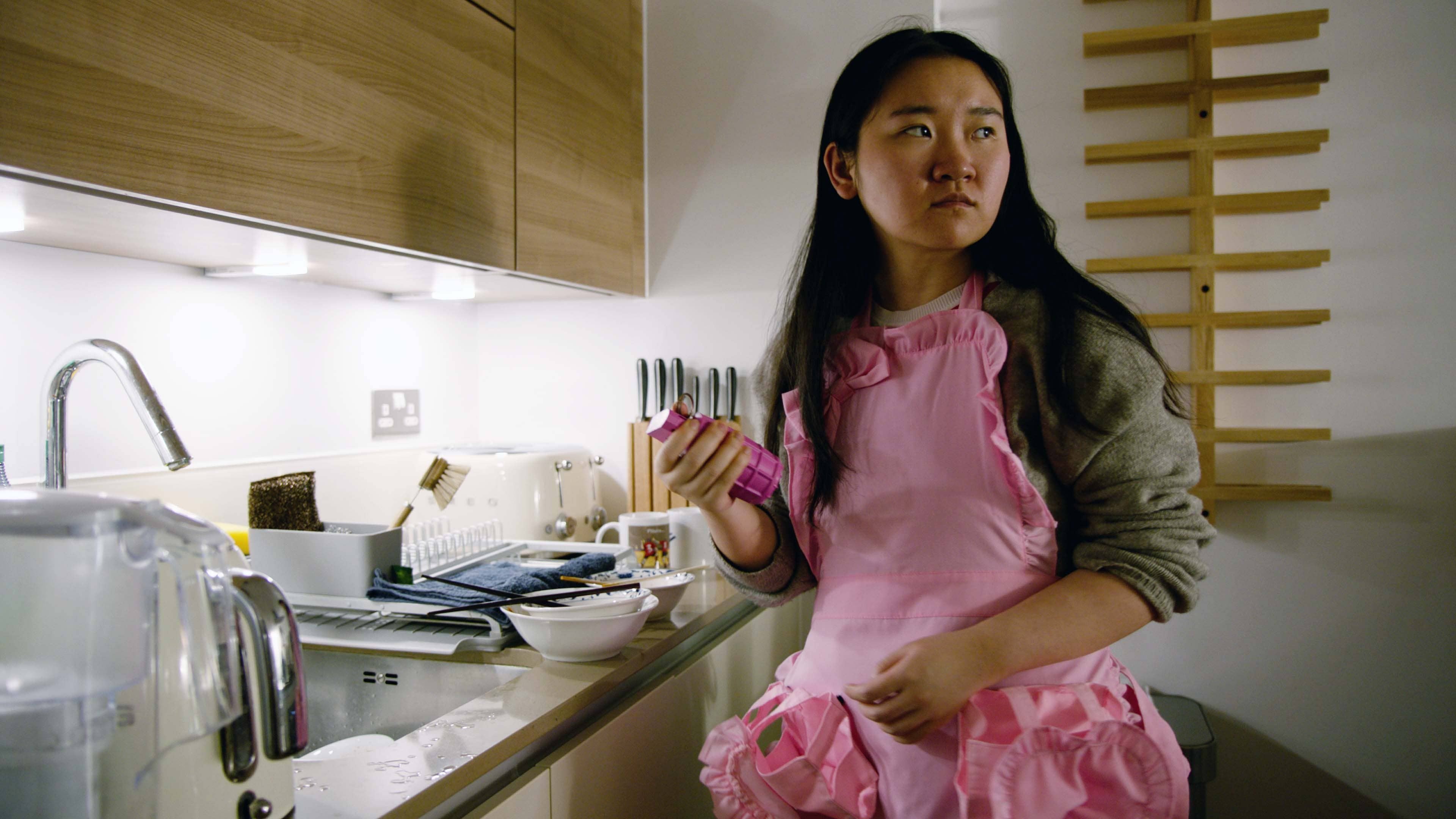 A person wearing a frilly pink apron holds a pink grenade.