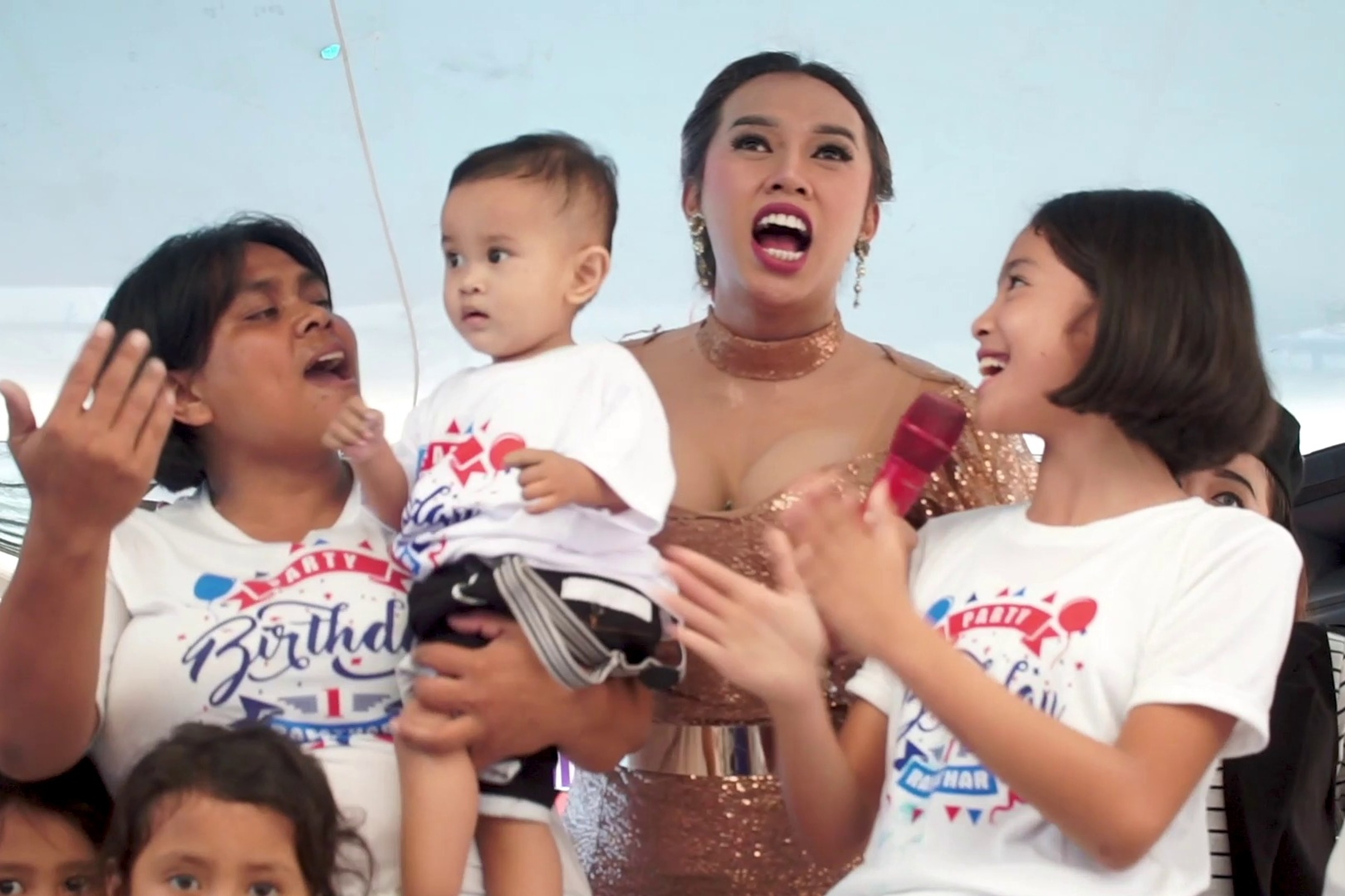 A performer in a sparkling outfit holding a young child while people beside them clap and sing.
