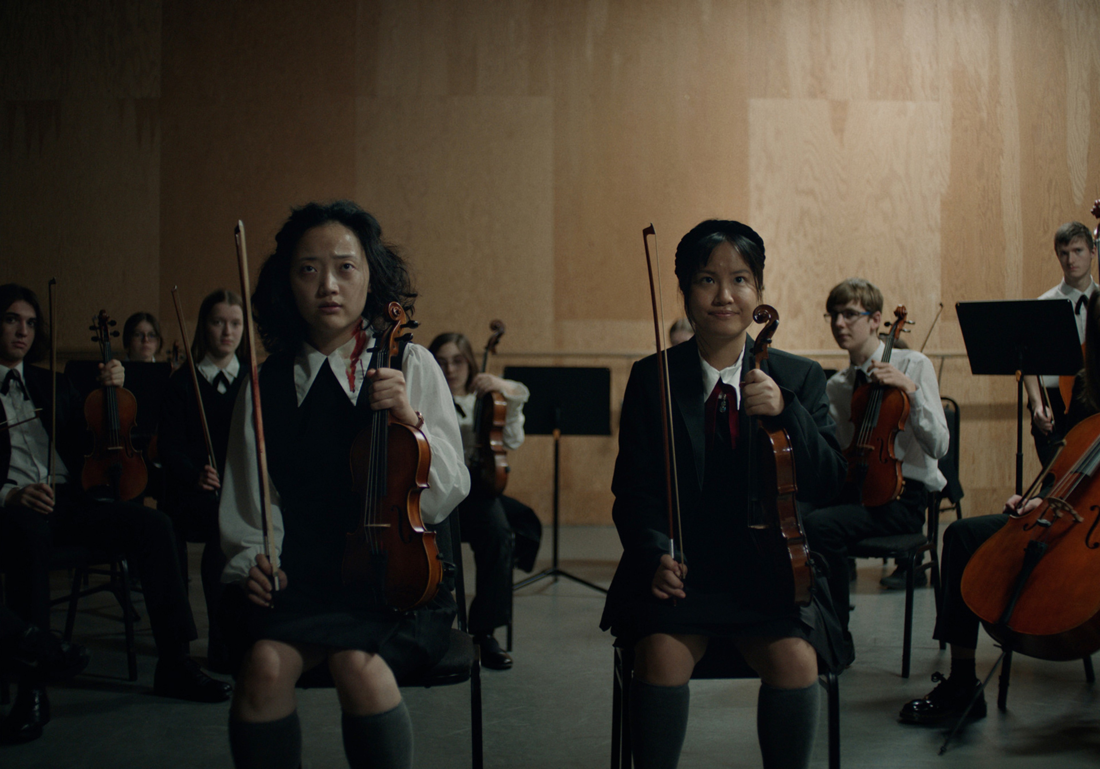 Two people holding violins sit side by side.