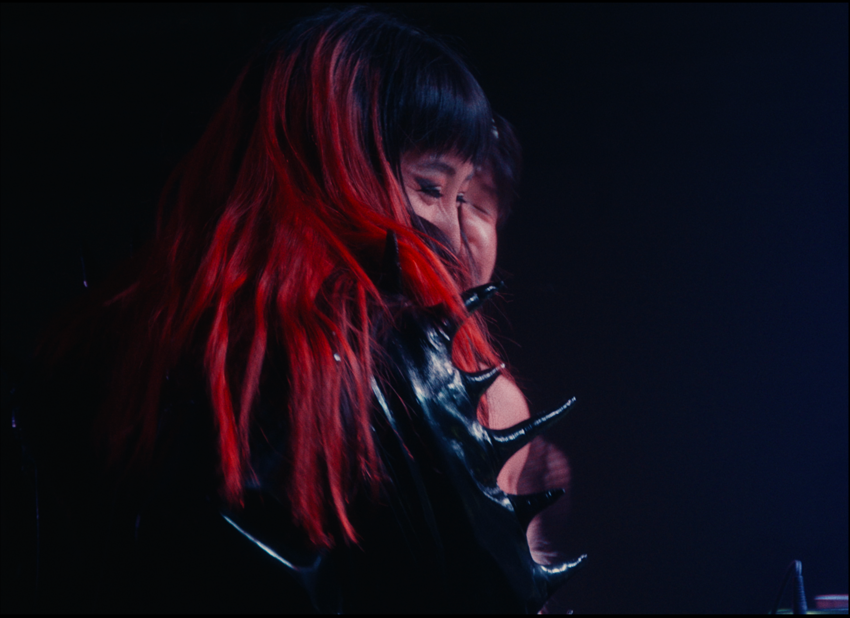 A person with long red hair wearing a spiky black outfit.