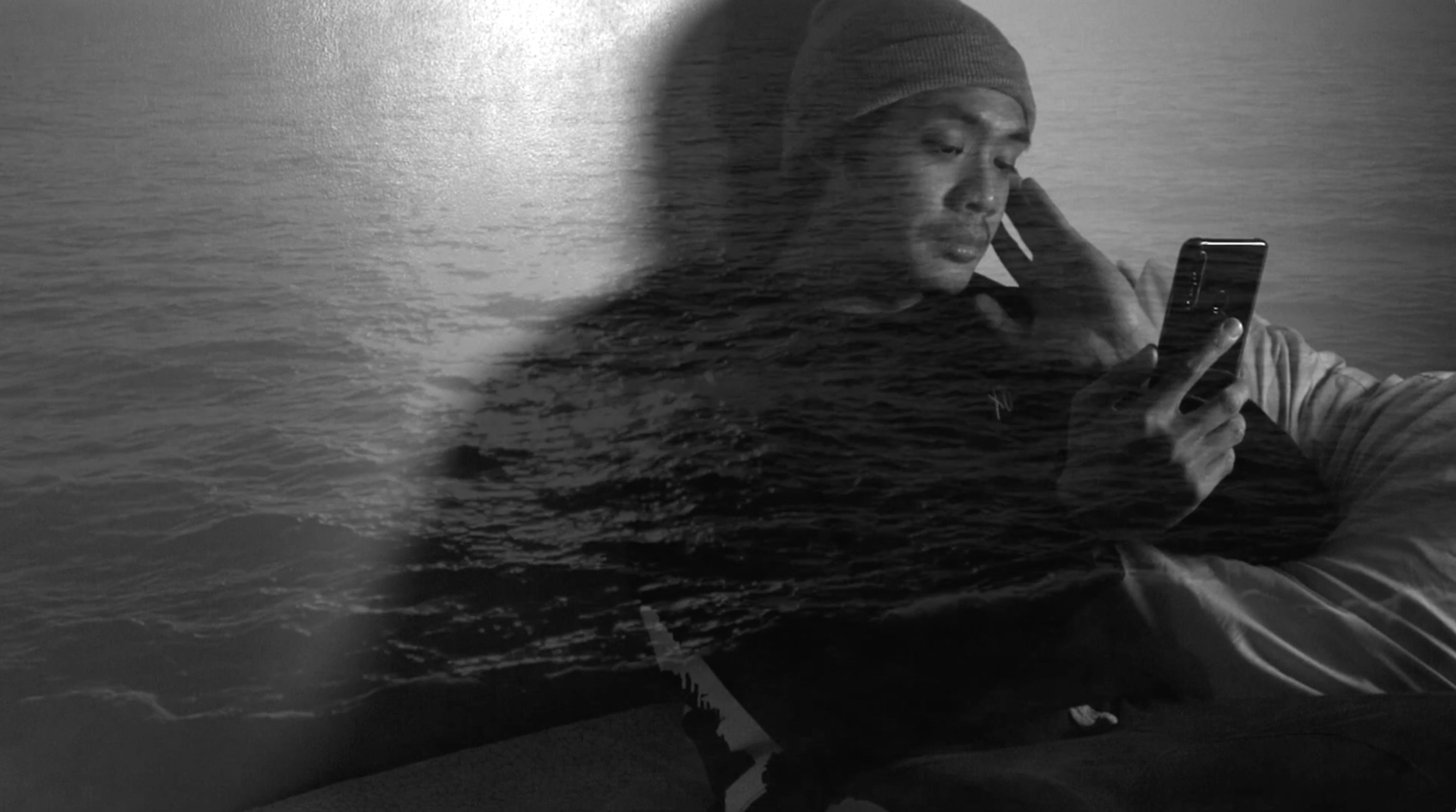 A person looking at their phone superimposed over the ocean.