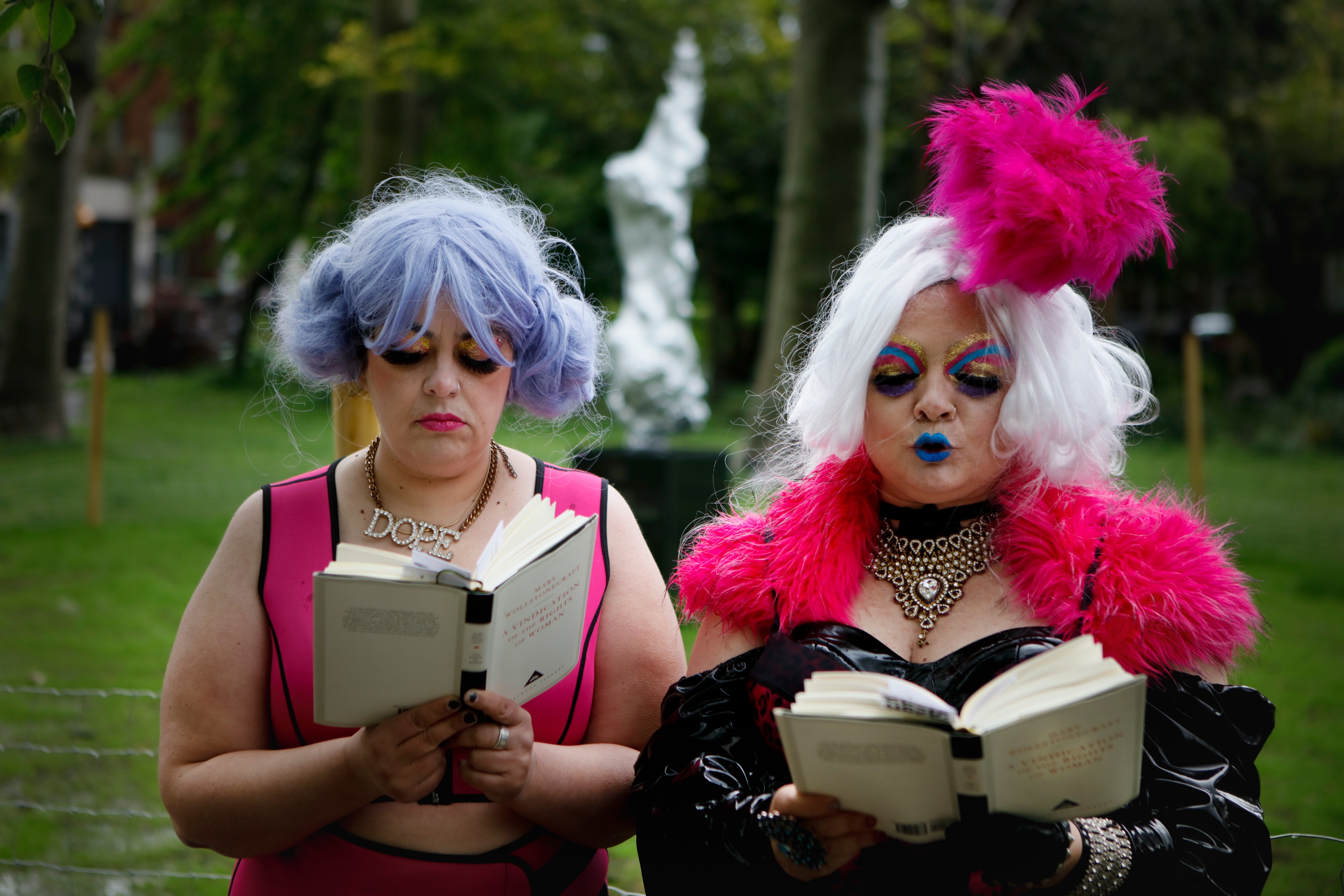Two figures stand side by side each reading a book.
