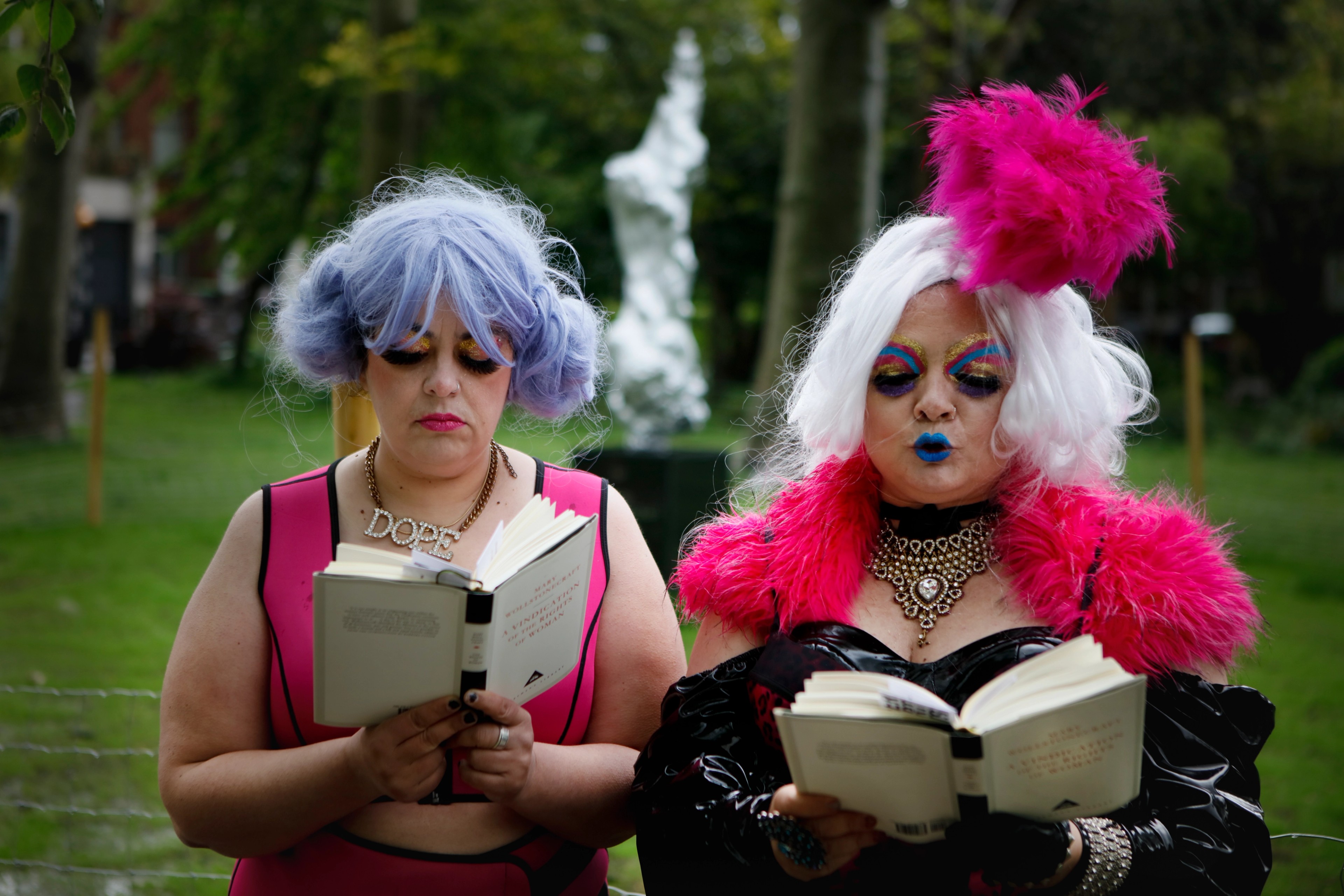 Two figures stand side by side each reading a book.