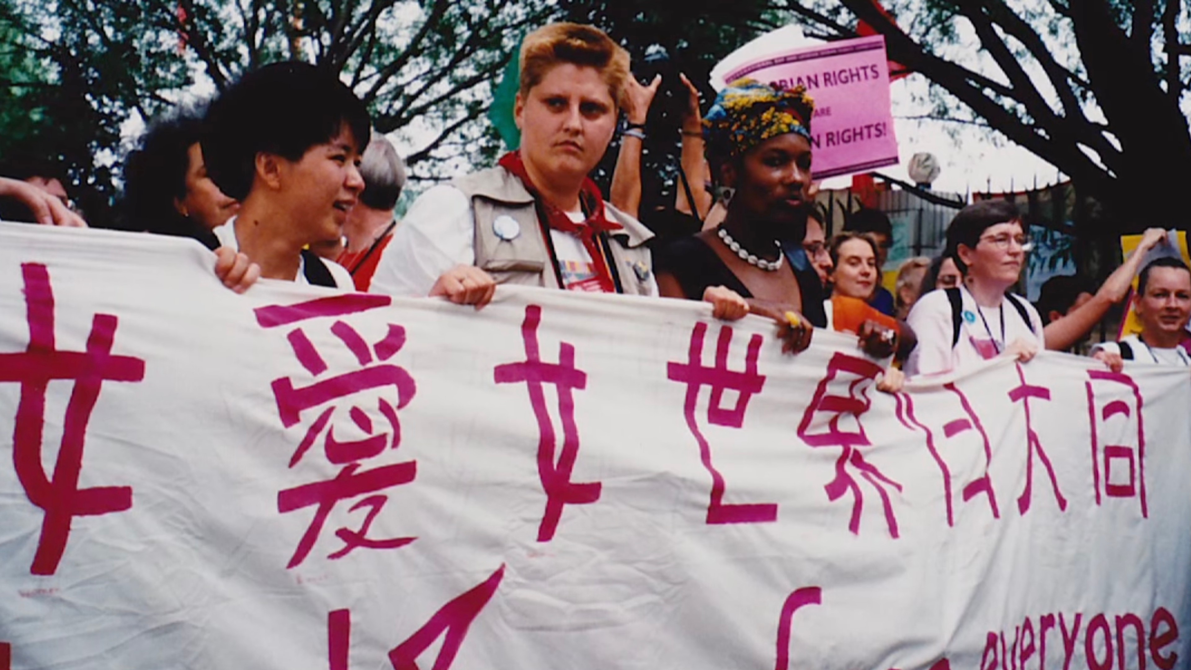 A group of people marching at a protest while holding a large banner with Chinese characters.