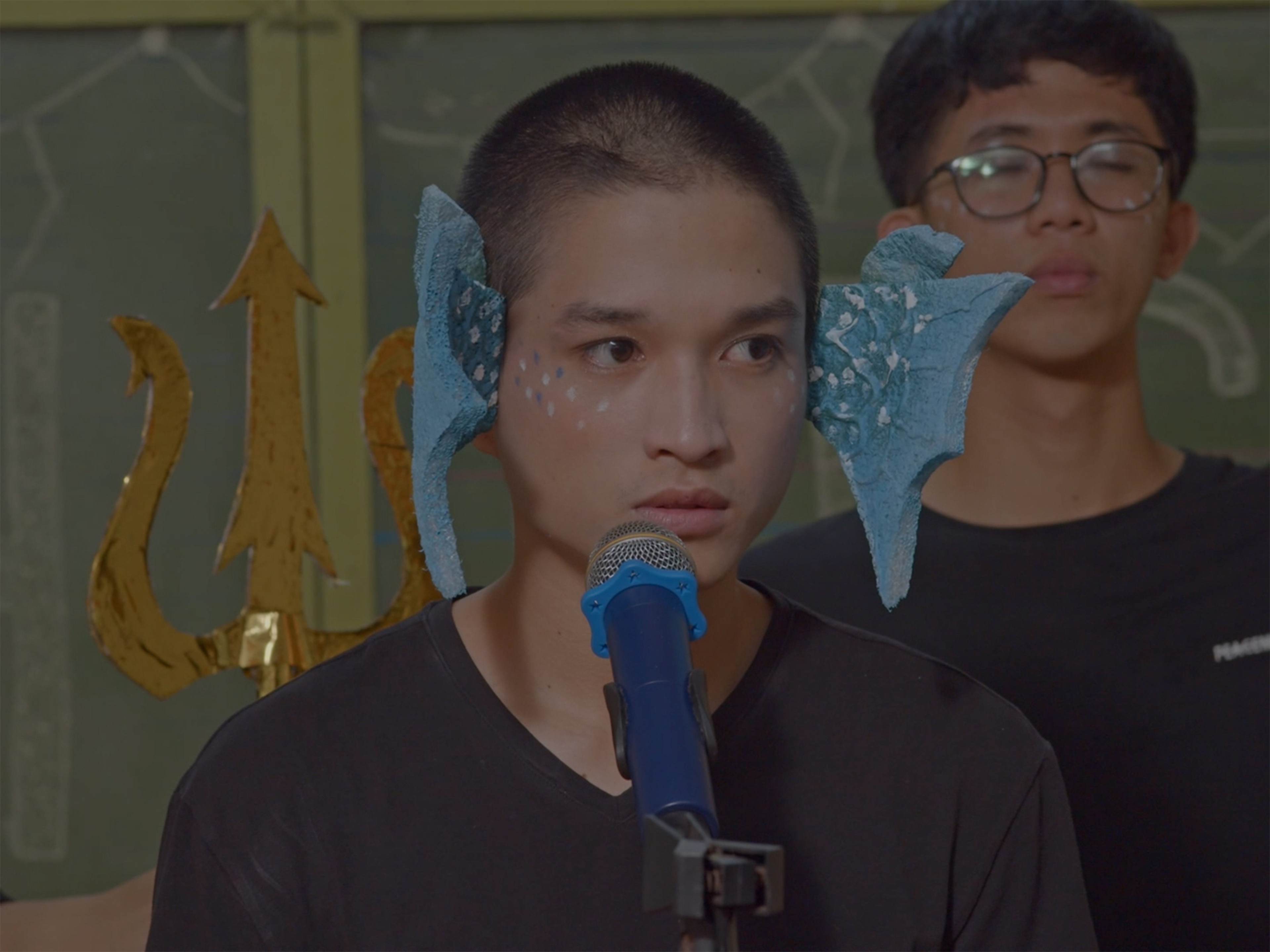 A person wearing blue fins on either side of their face in front of a microphone.