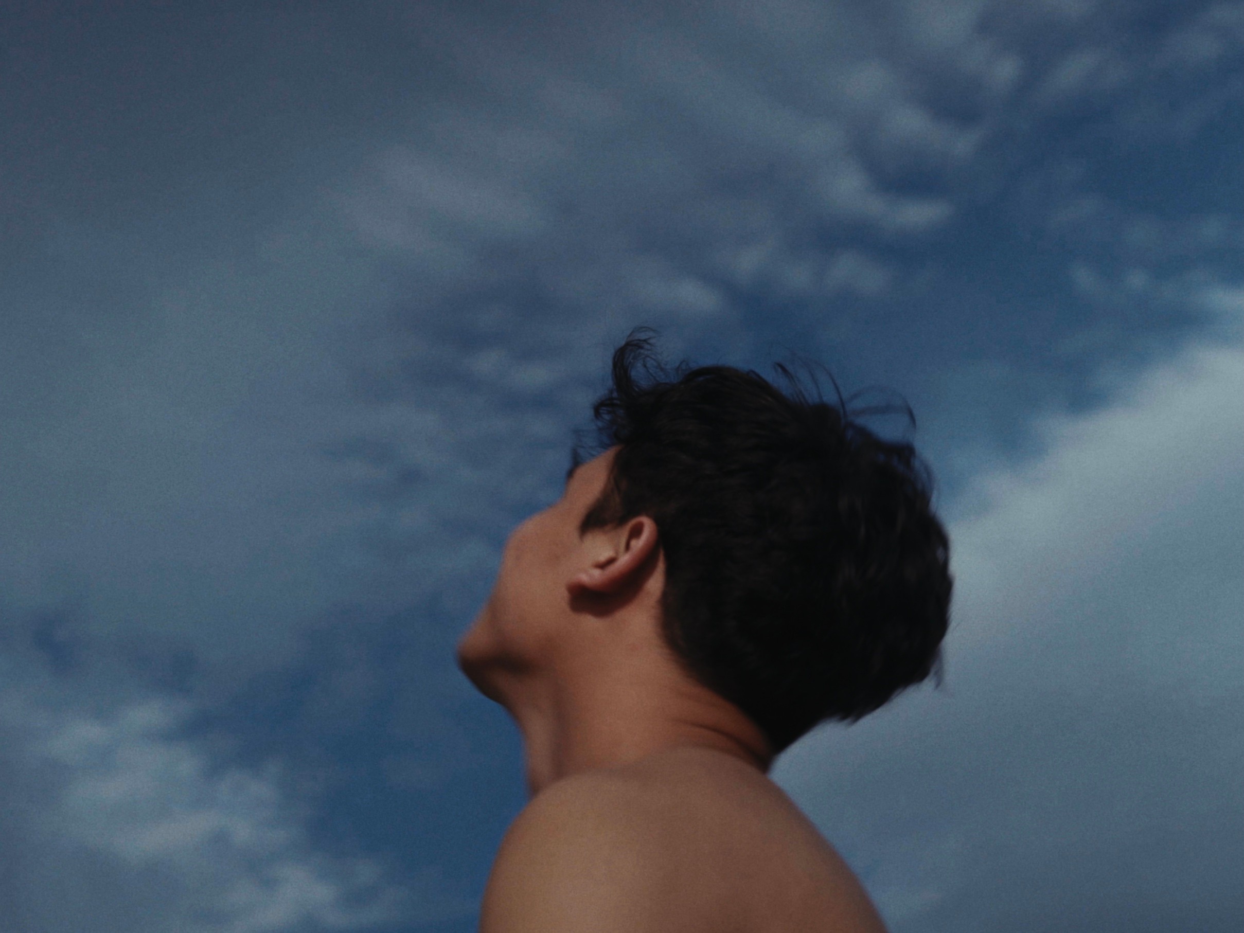 A shirtless person looking upward toward a cloudy blue sky.