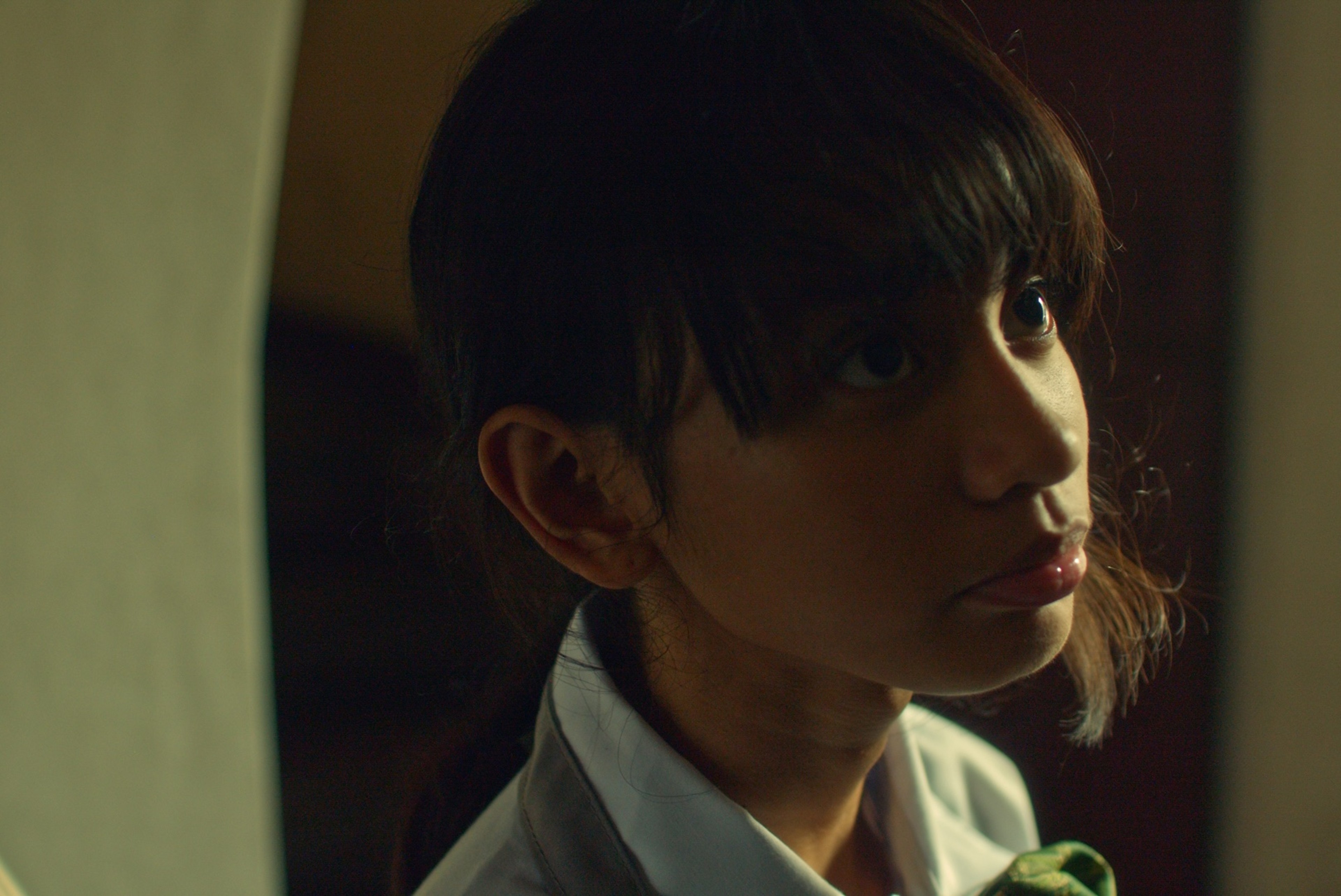 A young person in a school uniform looking upward in a dimly lit interior.